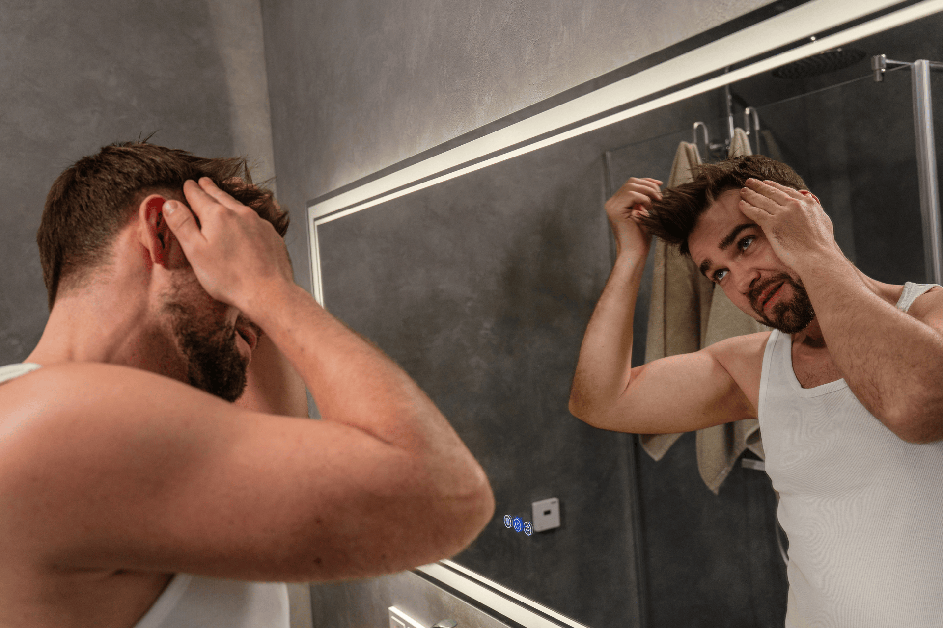 Man examining his hairline in the bathroom mirror, checking for signs of hair loss.