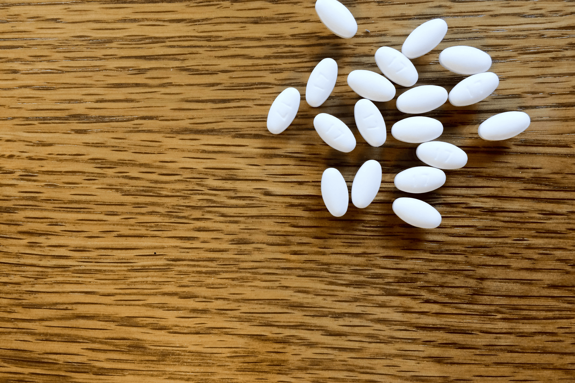 White oval pills scattered on a wooden surface.