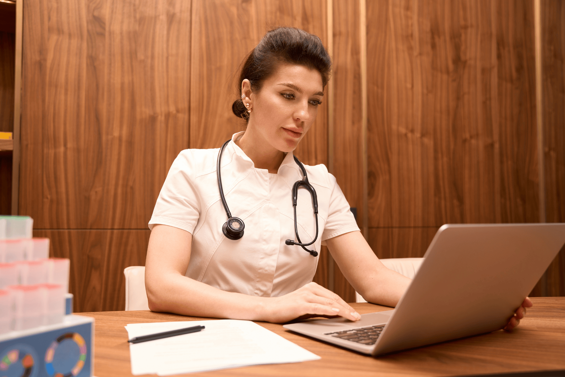 Female doctor in a white coat working on a laptop at her desk.
