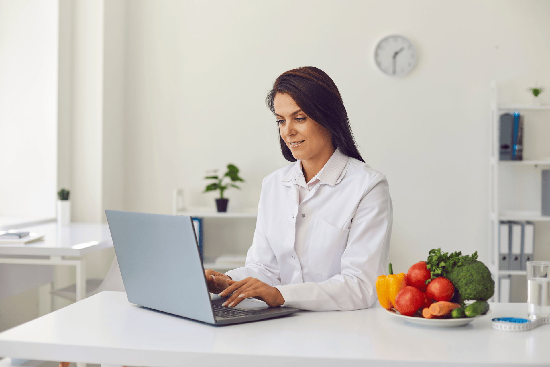 Female doctor working on a laptop with a plate of fresh vegetables beside her