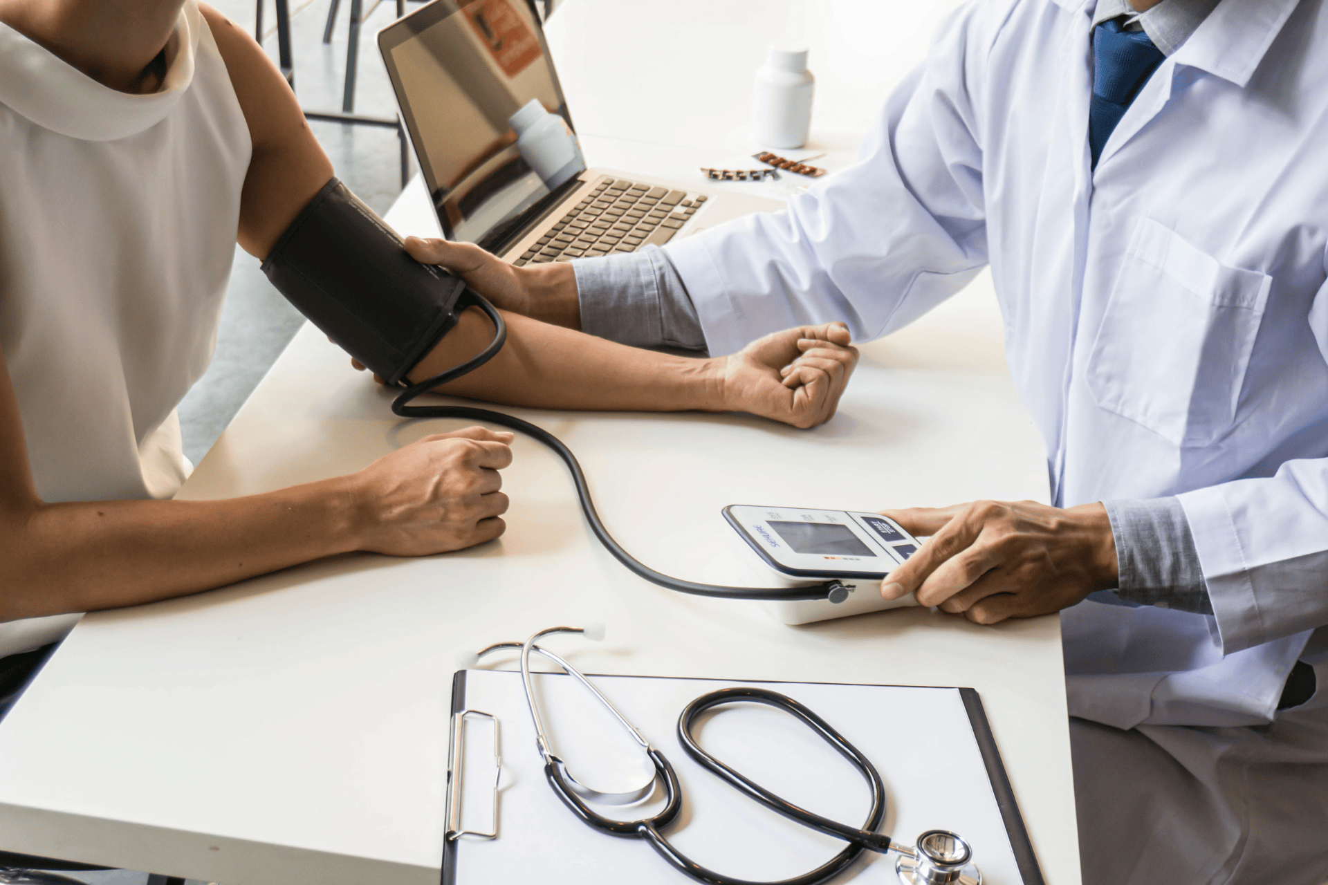 Doctor checking a patient’s arm with a blood pressure cuff on a clinic desk.