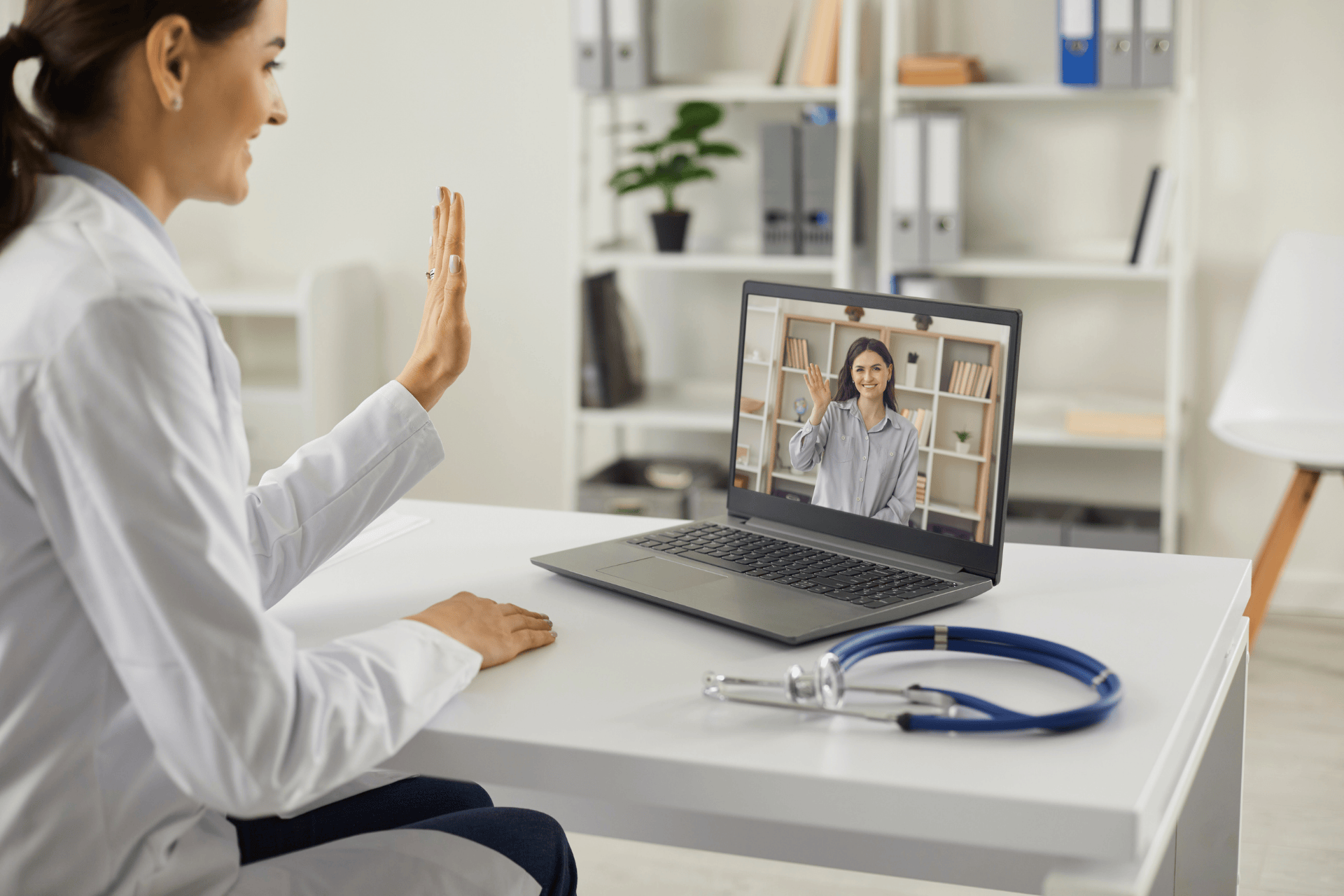 Doctor waving during a video call on a laptop.
