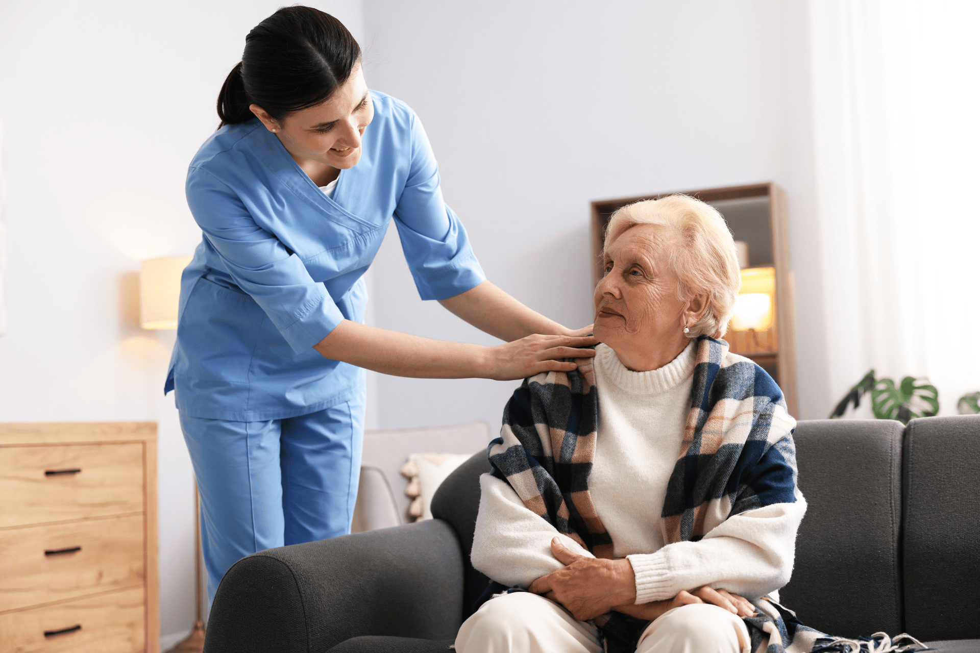 Nurse assisting an elderly woman sitting on a couch.