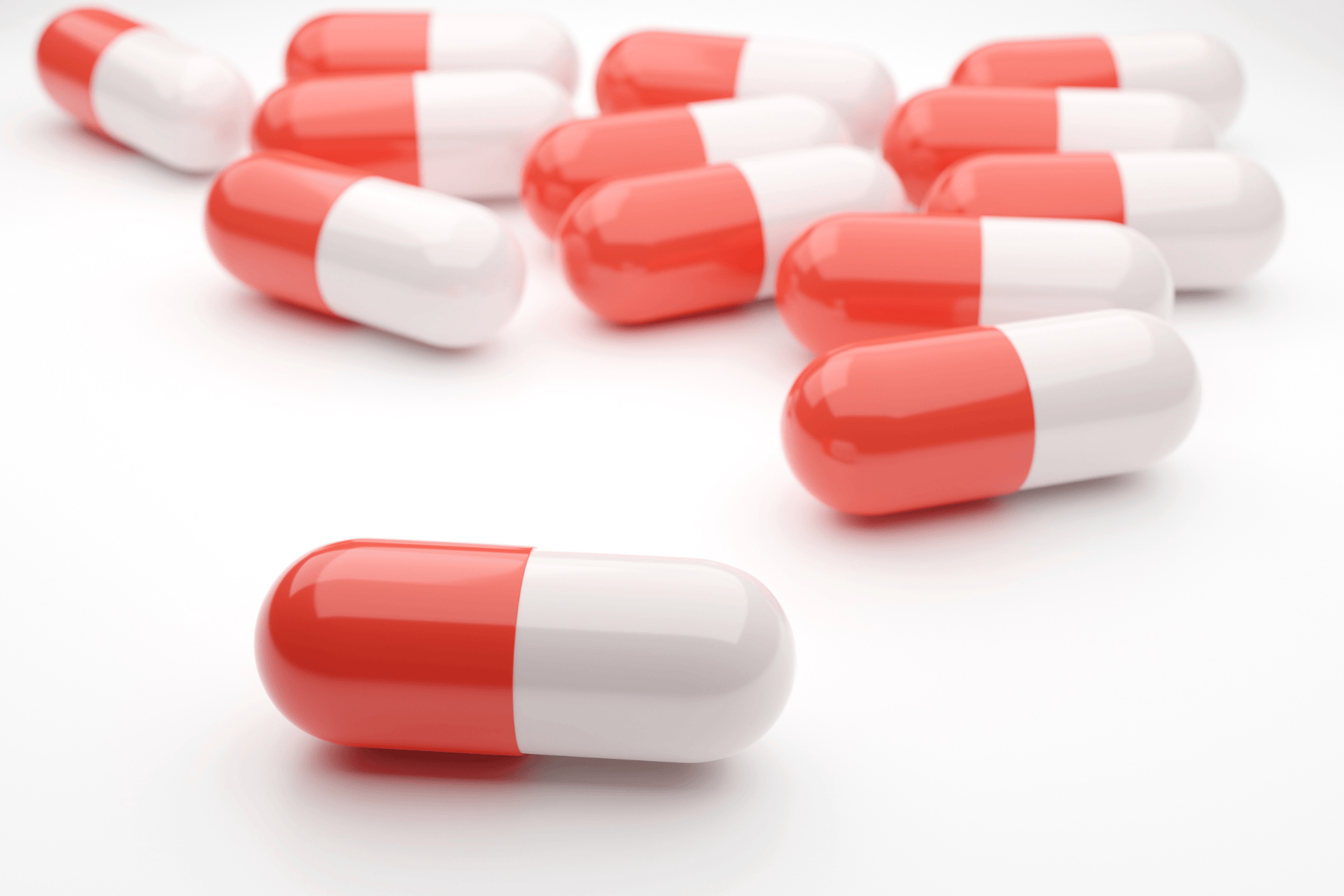 Close-up of red and white capsule pills on a white surface.