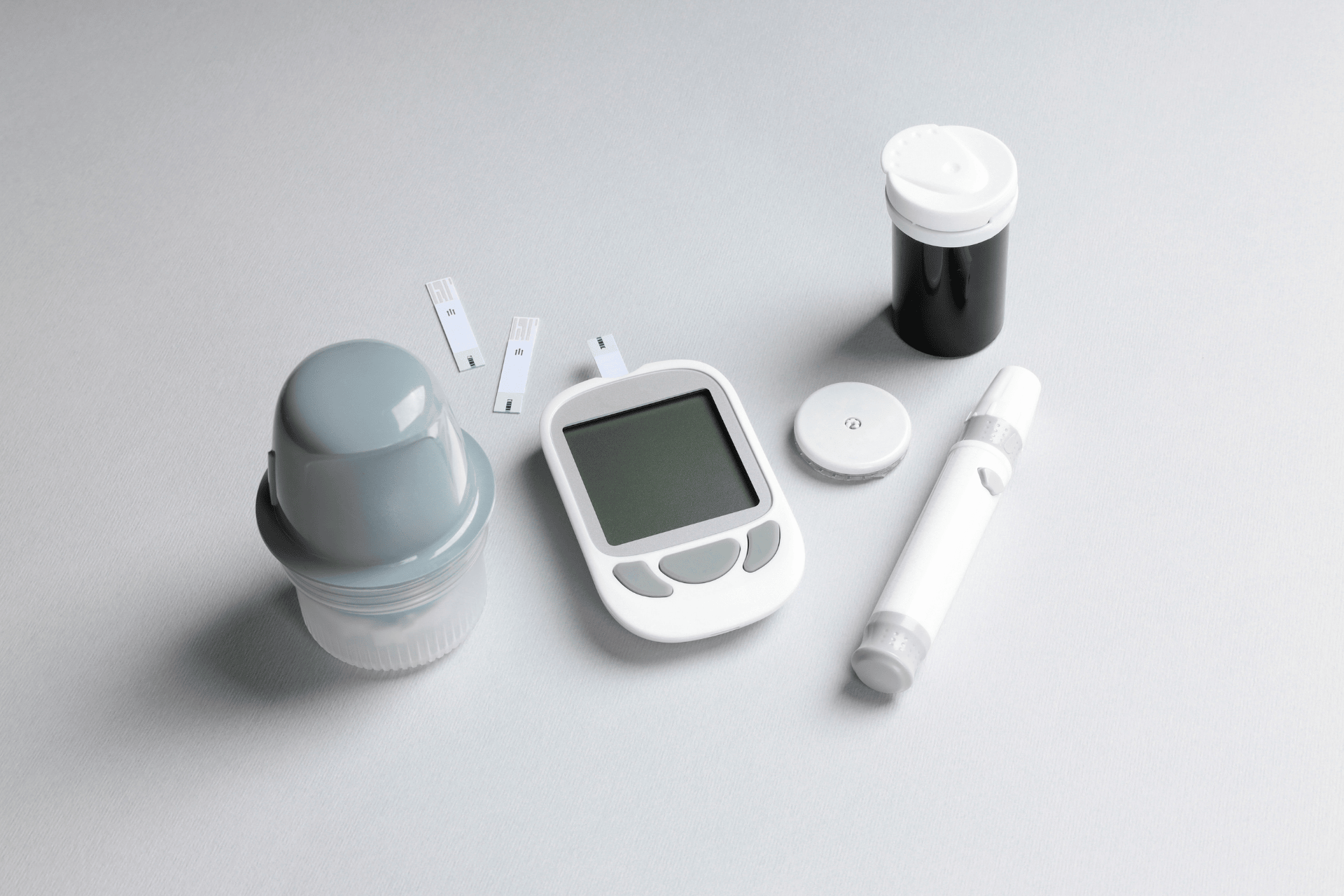 Blood glucose testing kit with a meter, test strips, lancet device, and supplies arranged on a light surface.