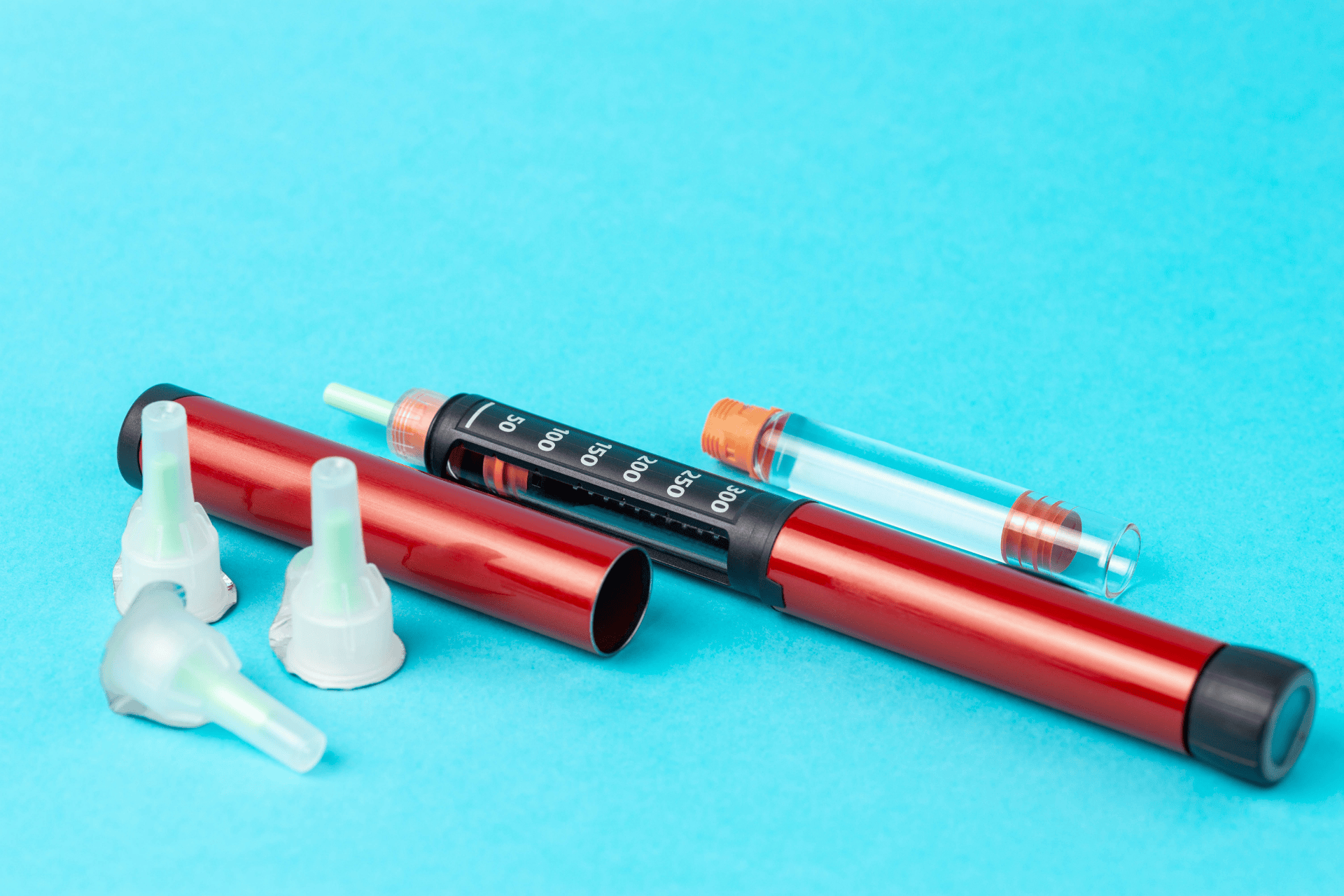 Red insulin pen with cartridge and needle caps on a blue background.