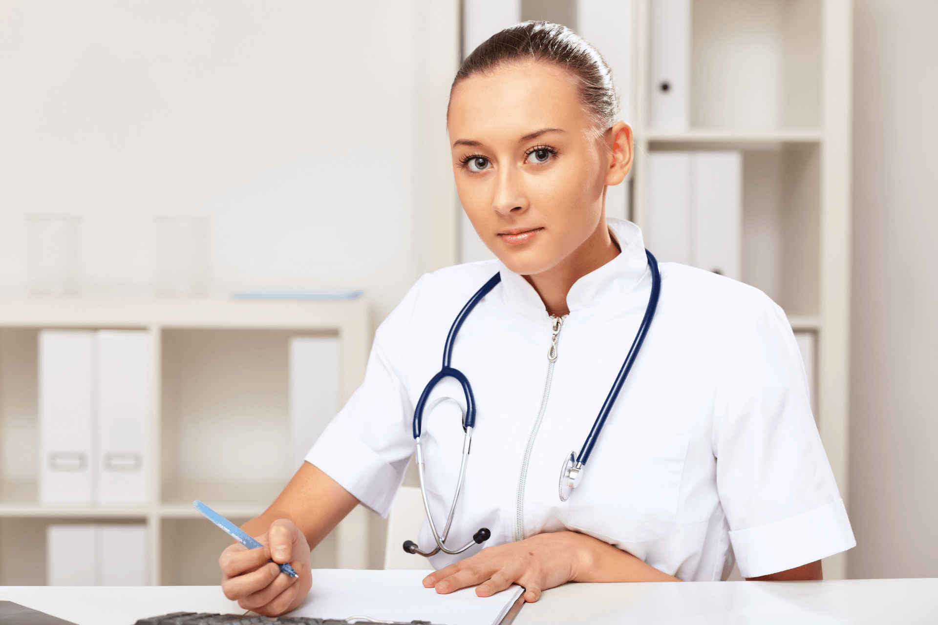 Female doctor with a stethoscope writing notes at her desk.