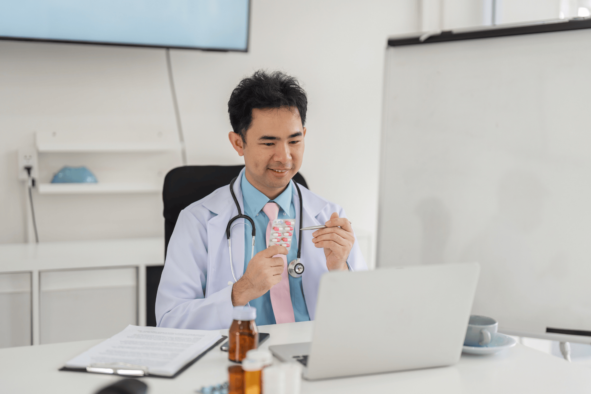 Doctor holding a pack of pills while speaking to a patient on a video call.