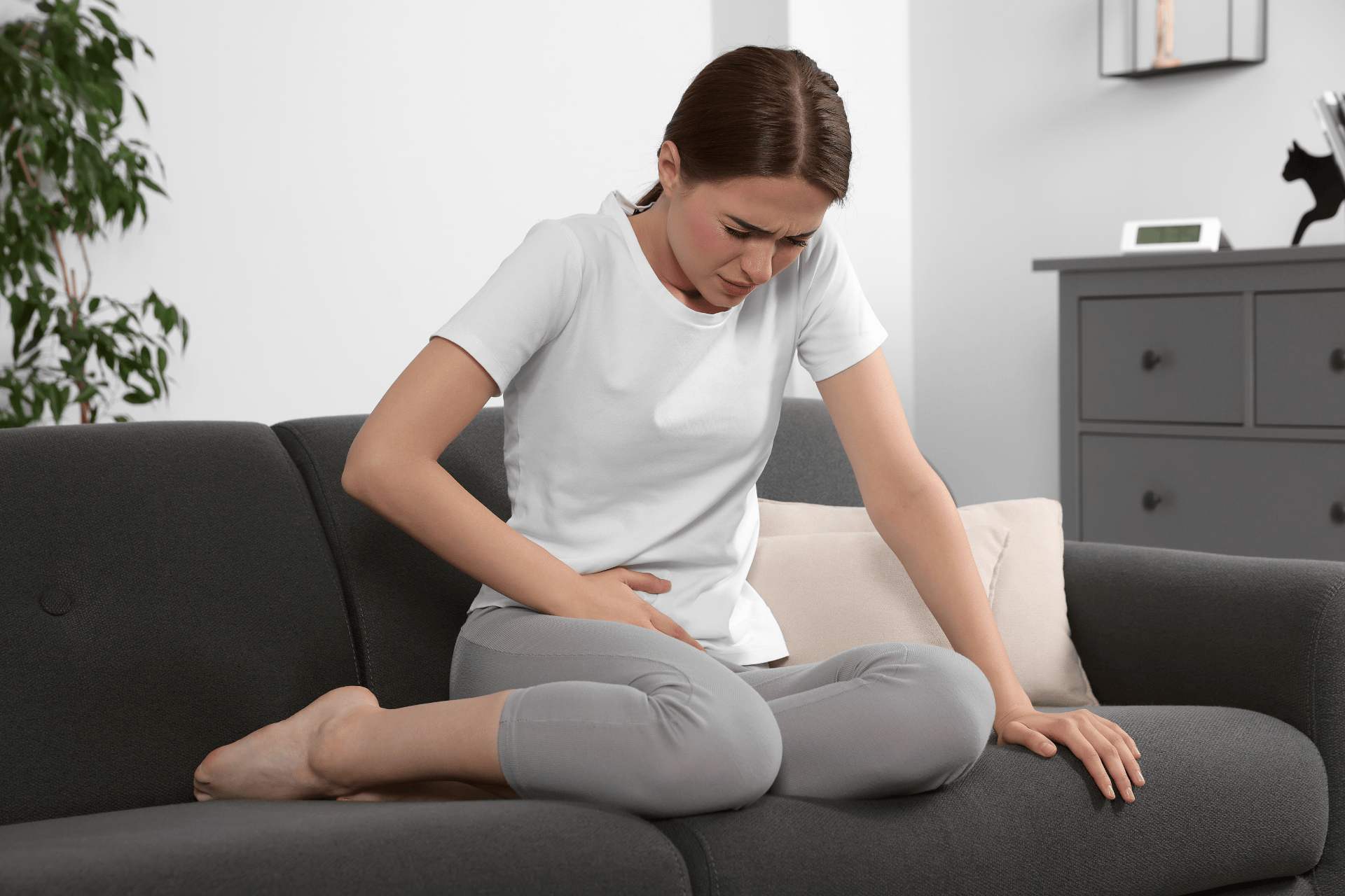 Woman sitting on a couch holding her lower abdomen in pain.