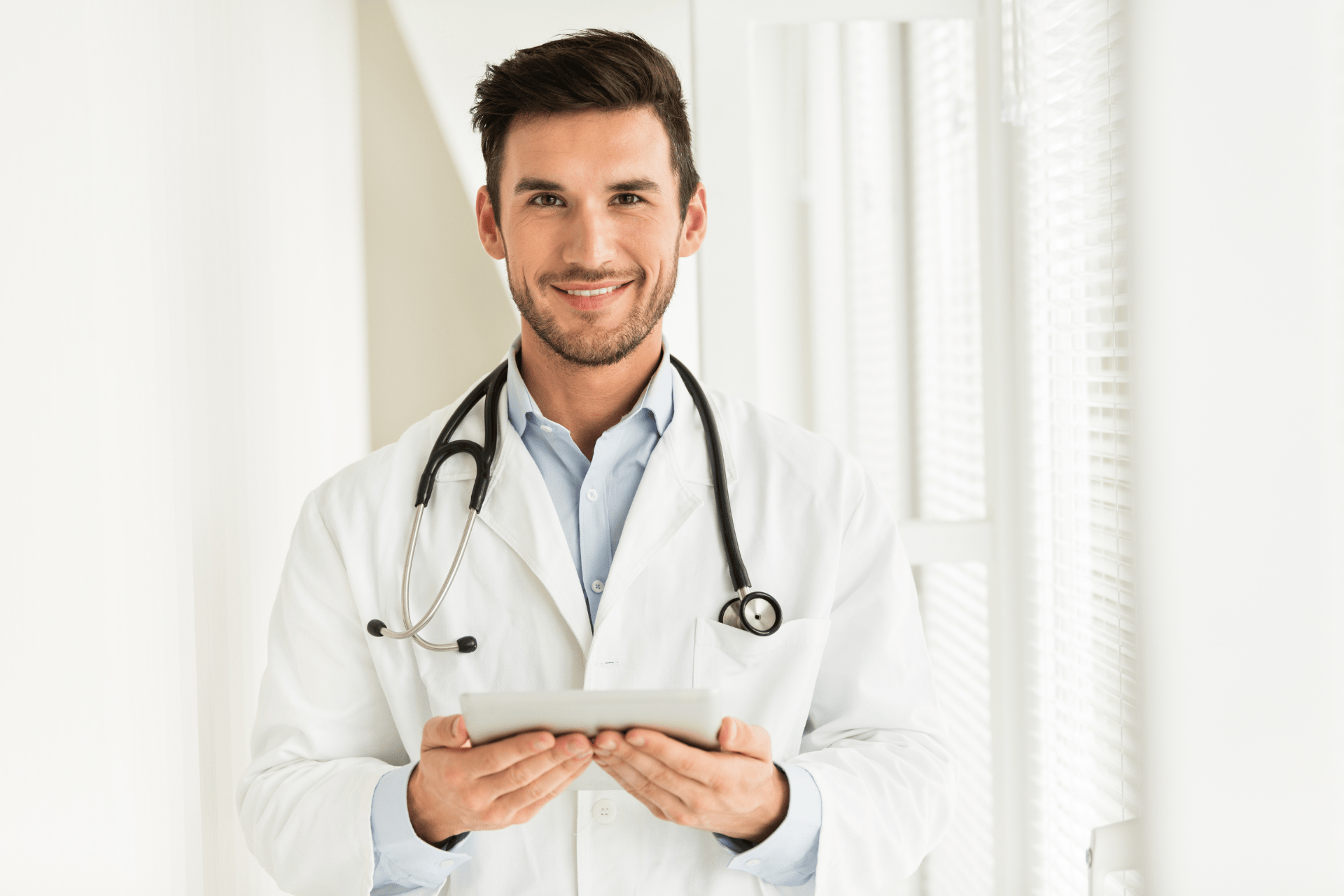 Smiling doctor holding a tablet with a stethoscope around his neck.
