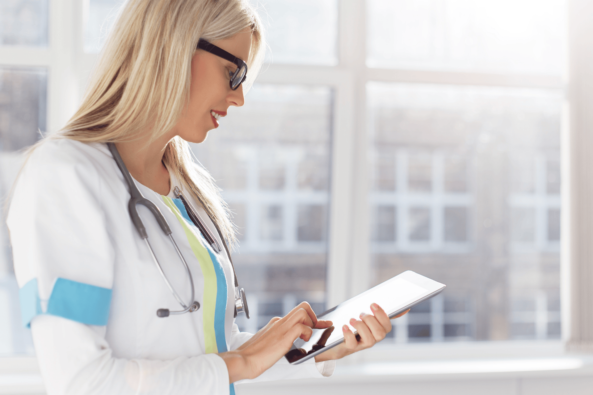 Female doctor using a tablet while standing in a bright medical office.