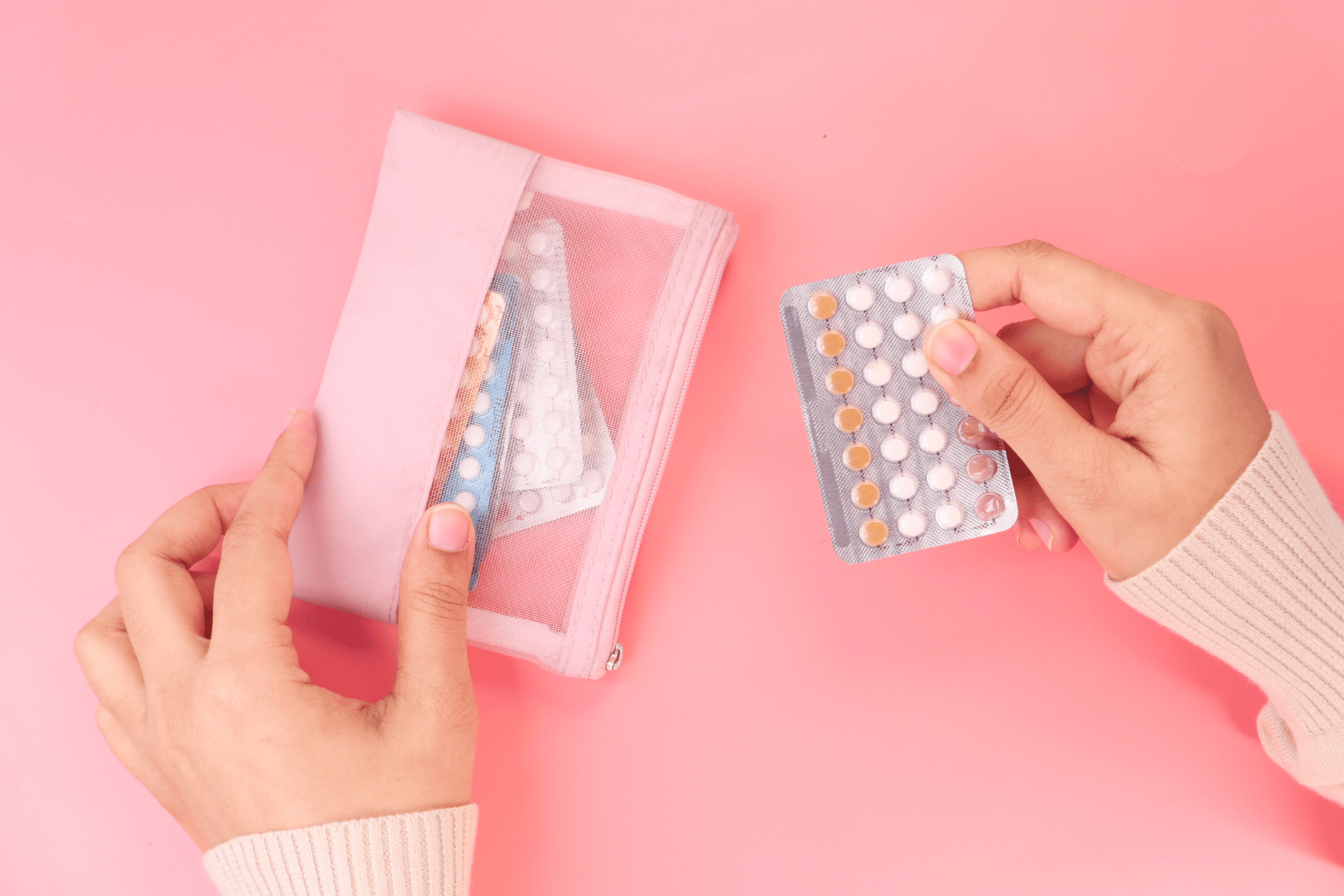 Hands holding a blister pack of birth control pills next to an open pink pouch with other pill packs