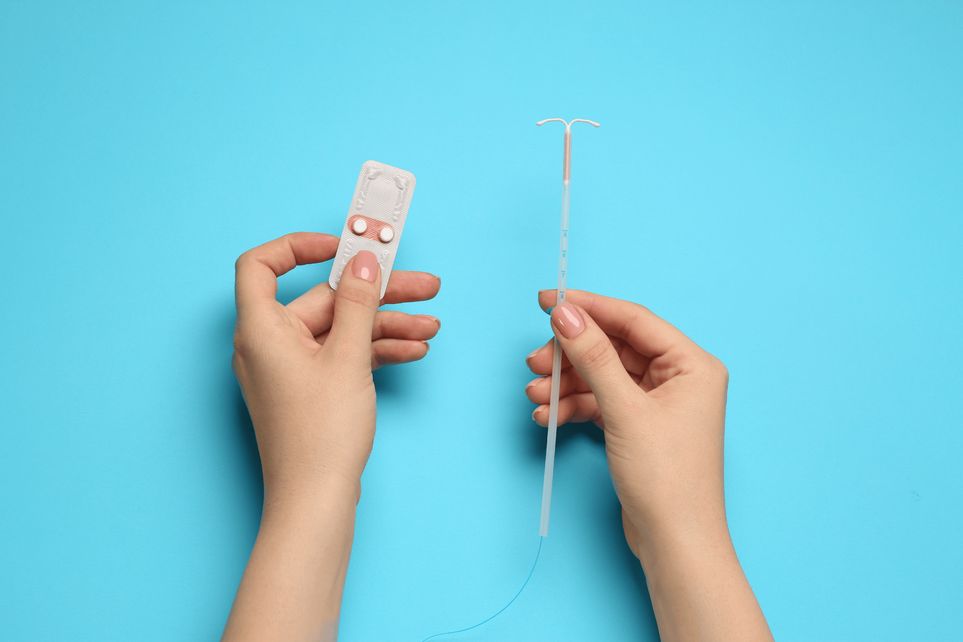 Hands holding an IUD device and a blister pack of pills on a blue background.