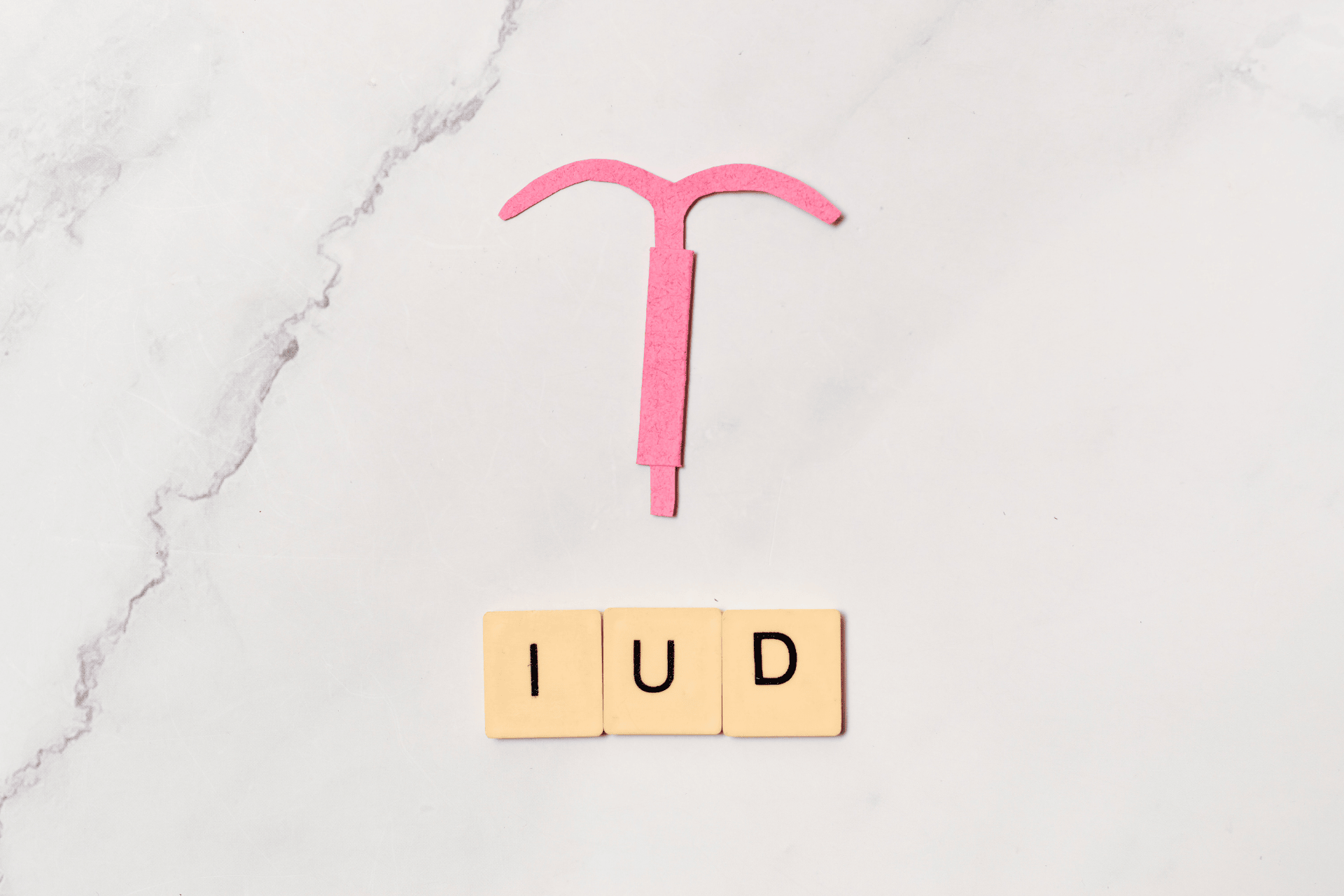 Pink IUD illustration placed above letter tiles spelling “IUD.