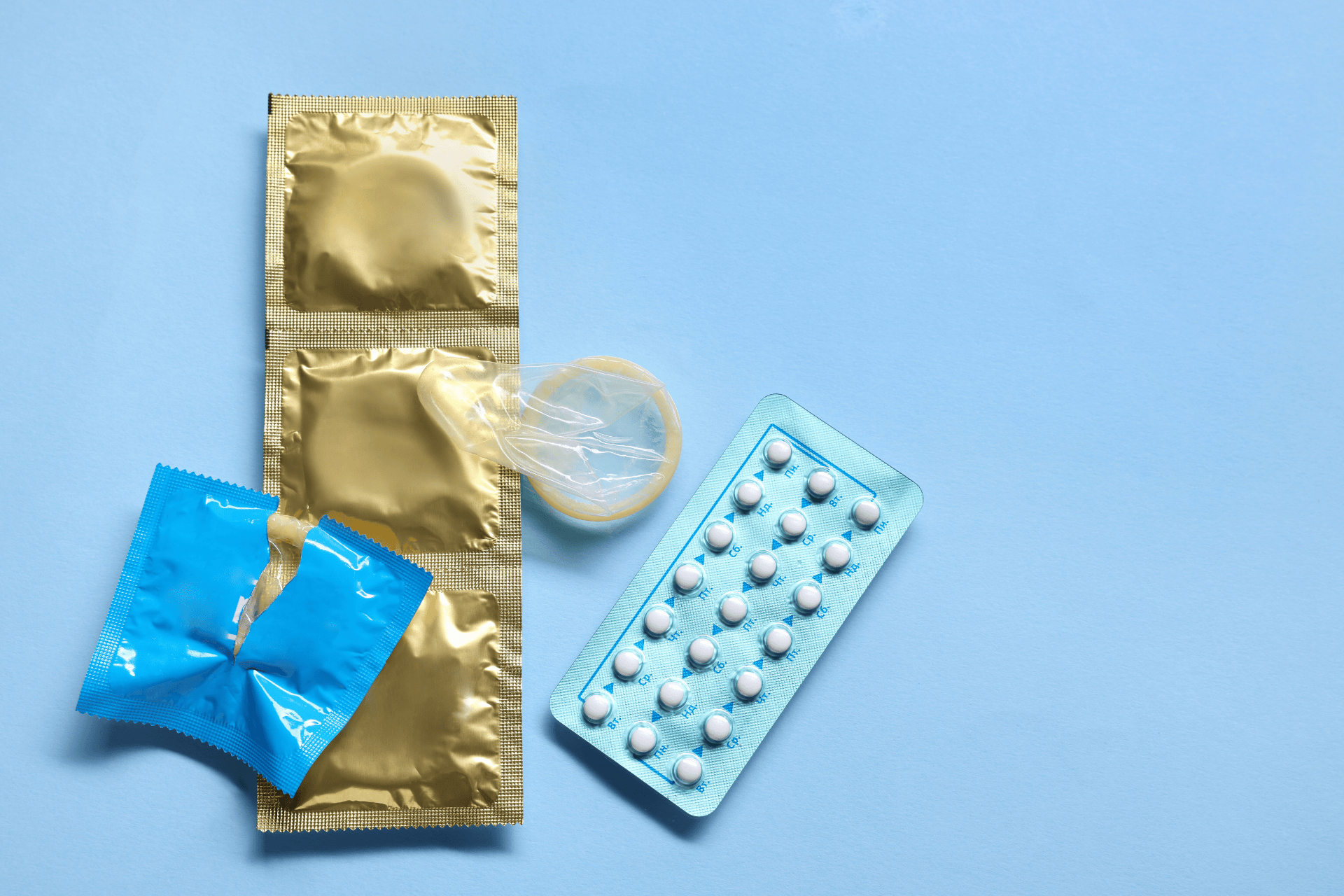 Condoms and a pack of birth control pills arranged on a light blue background.