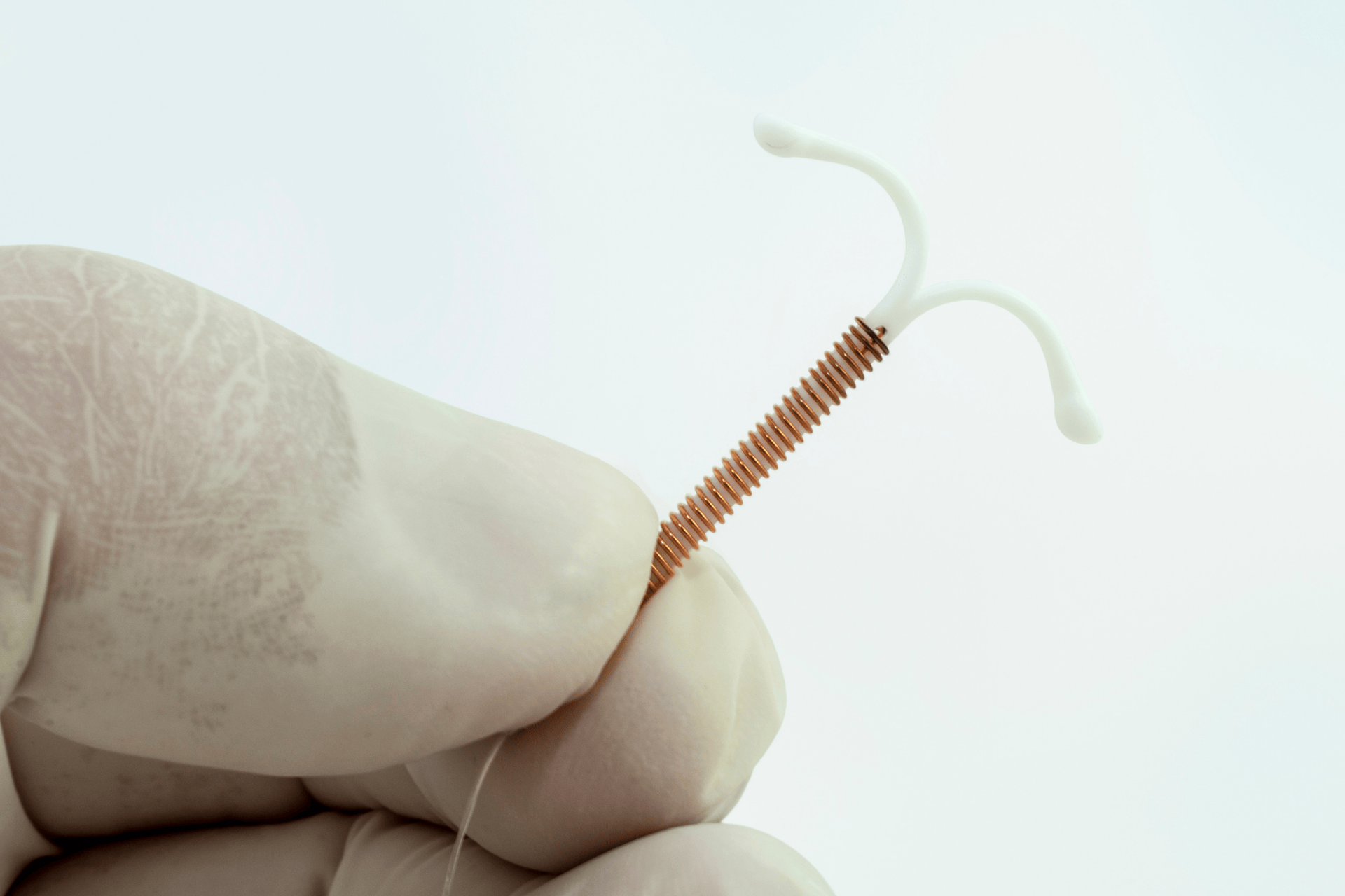 Gloved hand holding a copper IUD against a light background.