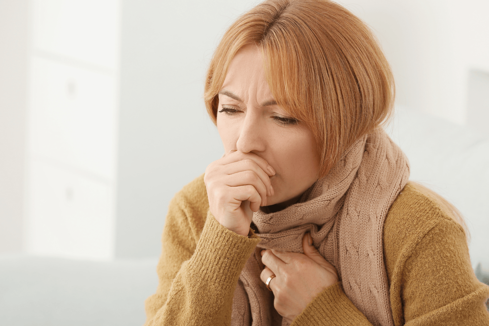 Woman coughing and holding her chest while wrapped in a scarf.