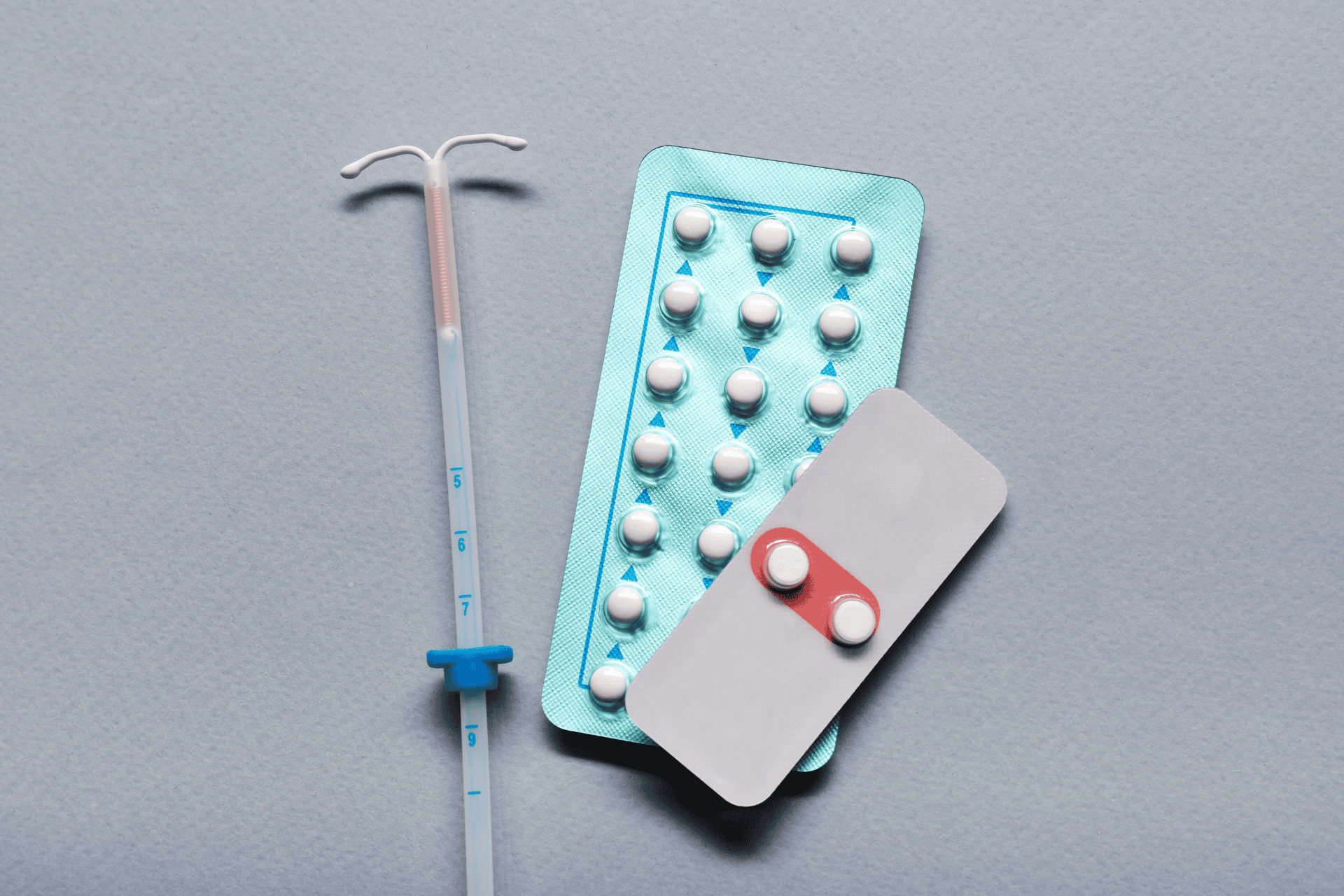 Birth control methods displayed on a surface, including an IUD and blister packs of pills.
