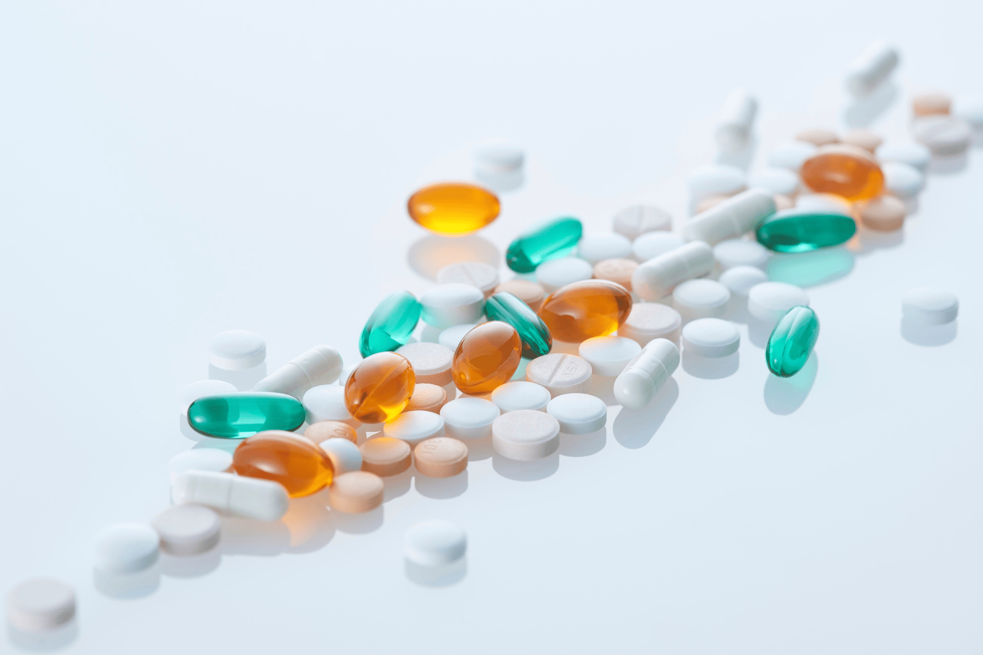 Various pills and capsules in different colors scattered on a reflective surface