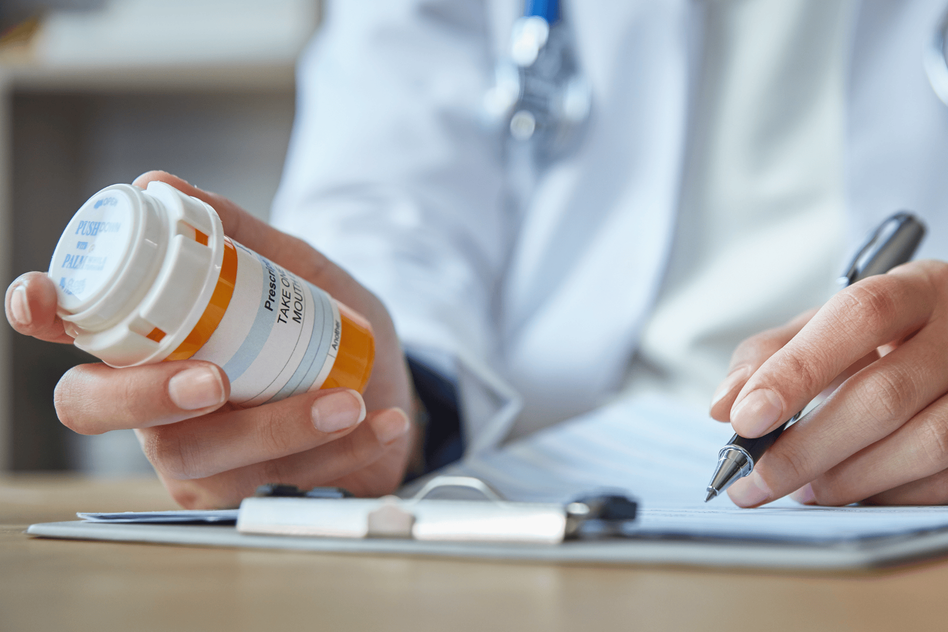 Hand holding a prescription pill bottle while writing notes on a clipboard