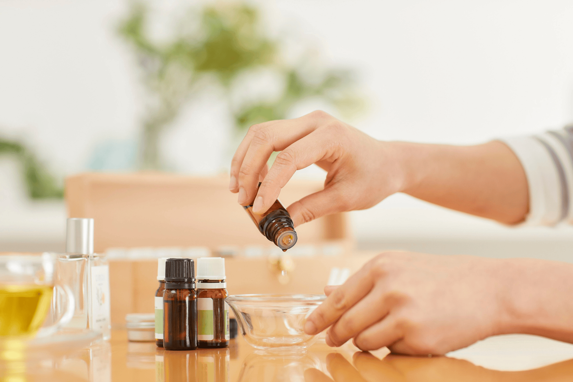 Person pouring essential oil into a small bowl, with bottles of oils on the table, used for eczema care.