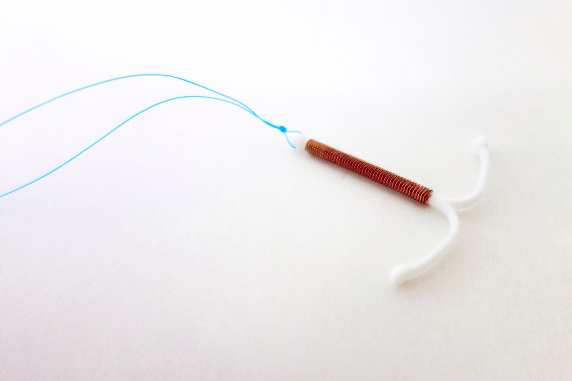 Copper IUD birth control device with blue strings on a white background.