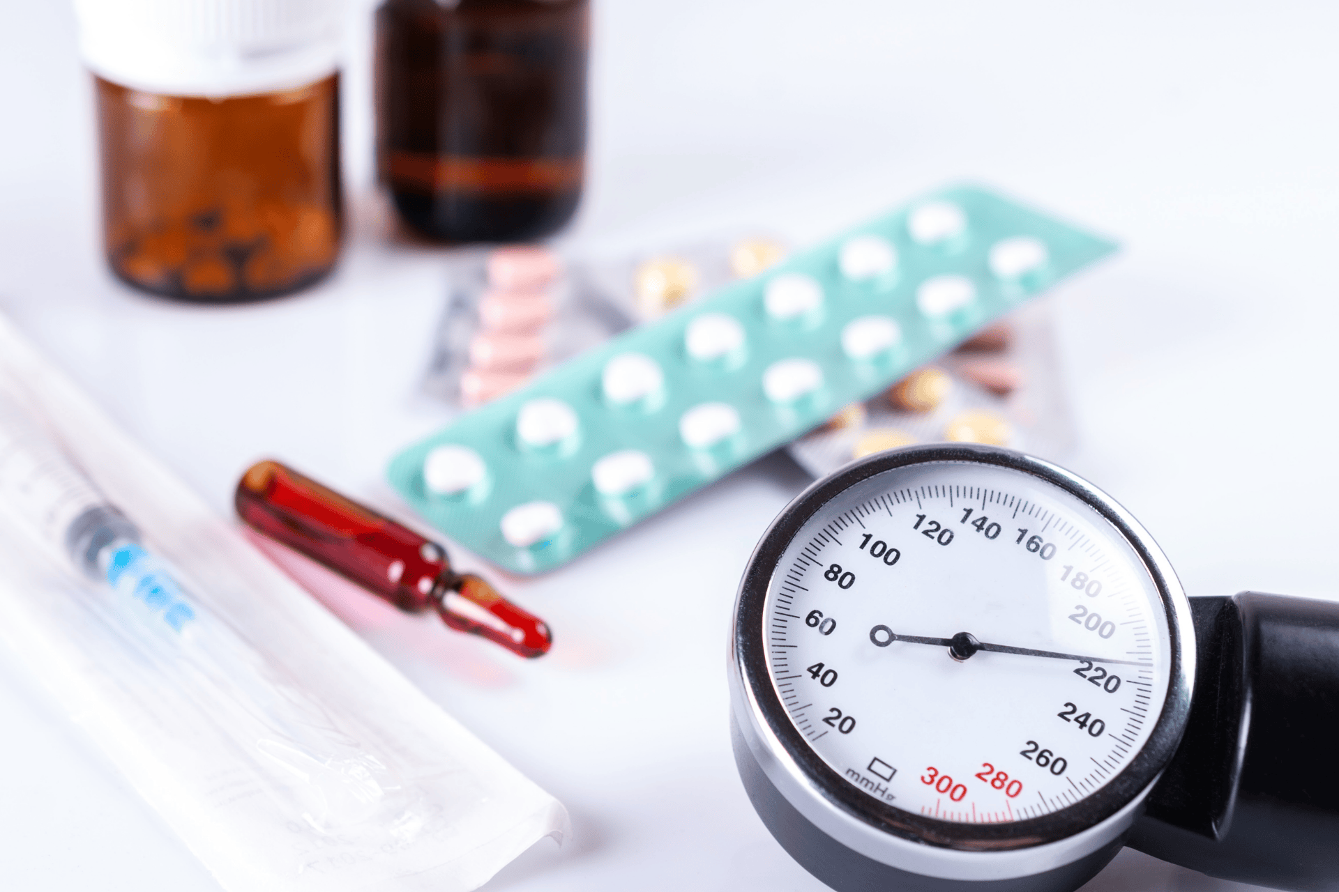Blood pressure gauge surrounded by various medications, including blister packs, pill bottles, a syringe, and an ampoule.