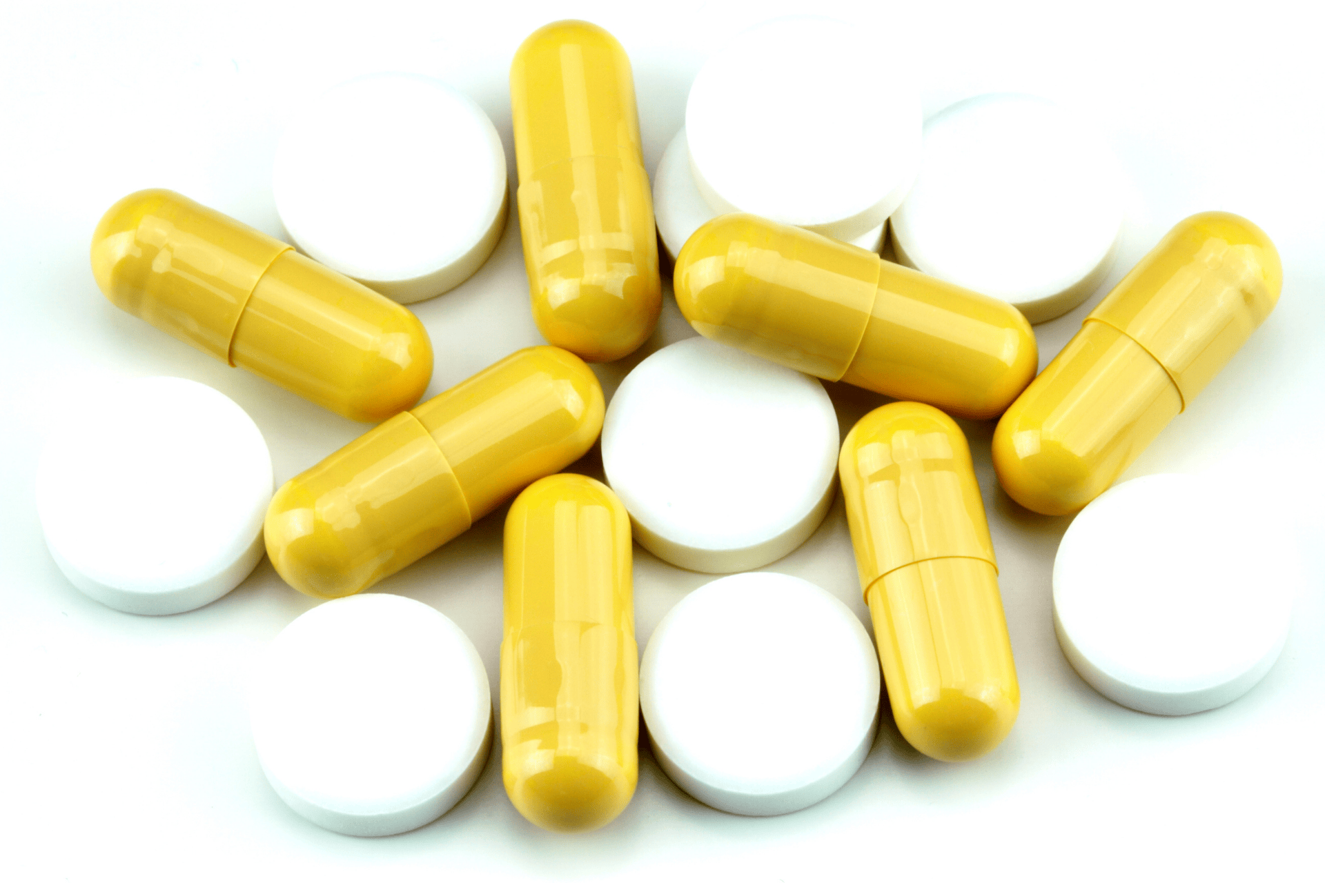 A close-up of yellow capsules and round white tablets scattered together on a white surface.
