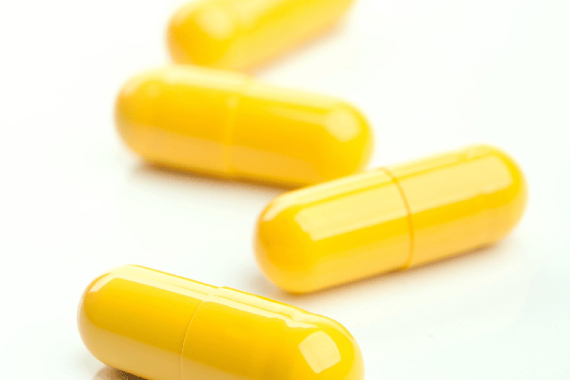 Close-up of bright yellow medicine capsules on a white surface.