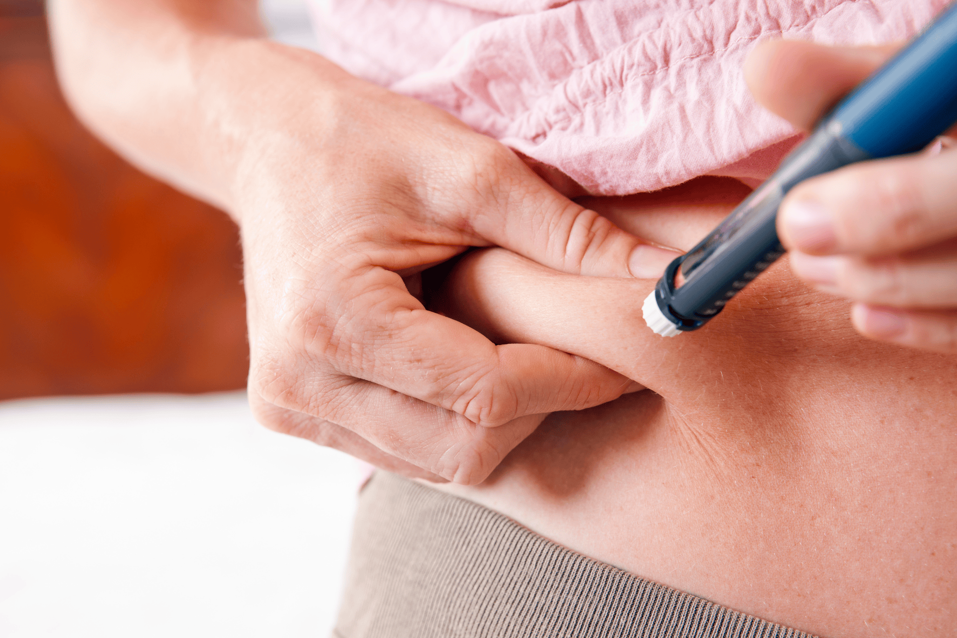Close-up of a person pinching the skin on their abdomen while using an insulin pen to give themselves an injection.