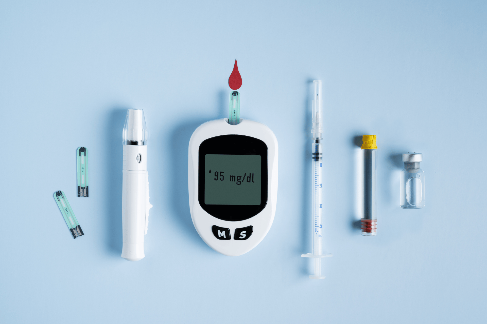 A blood glucose meter displaying a reading, with lancets, test strips, syringes, and vials arranged on a blue background.