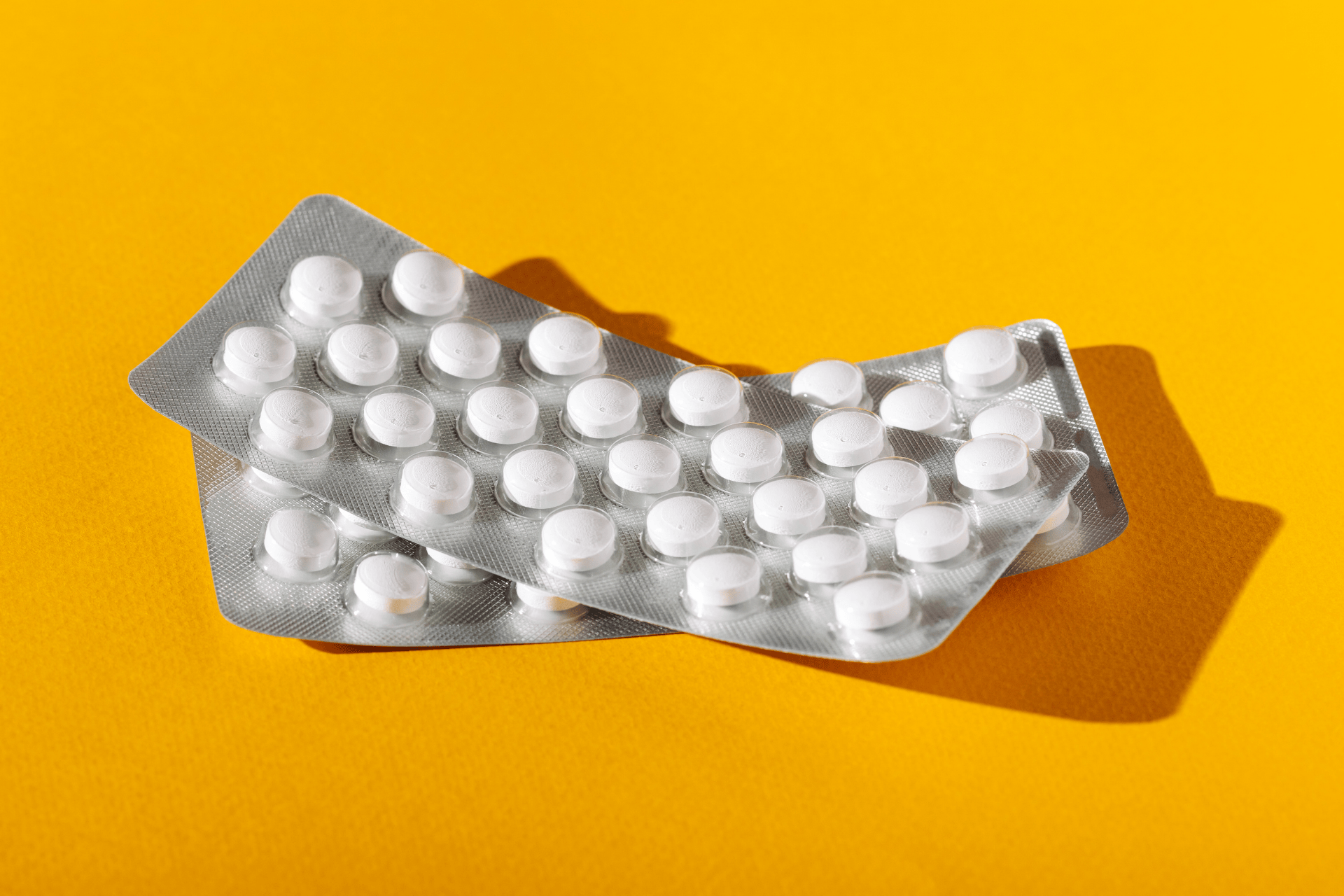 Blister packs of white tablets on a yellow background.