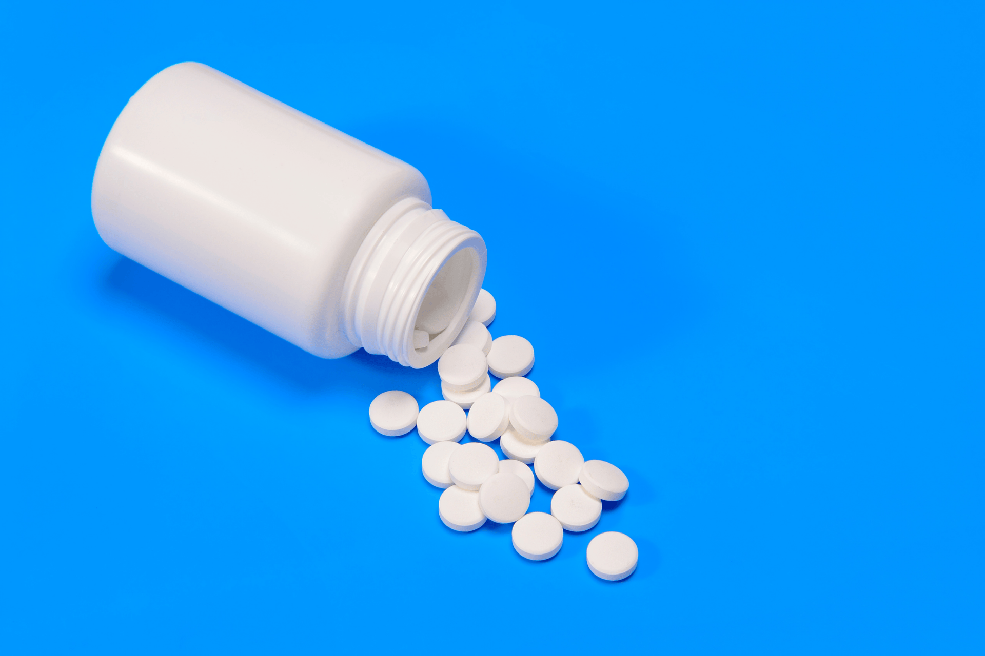 White pill bottle tipped over, tablets spilling onto a blue surface.