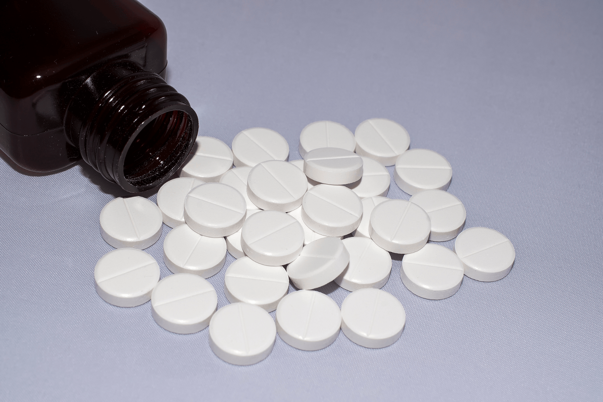 Brown medicine bottle tipped over, spilling white round tablets onto a flat surface.