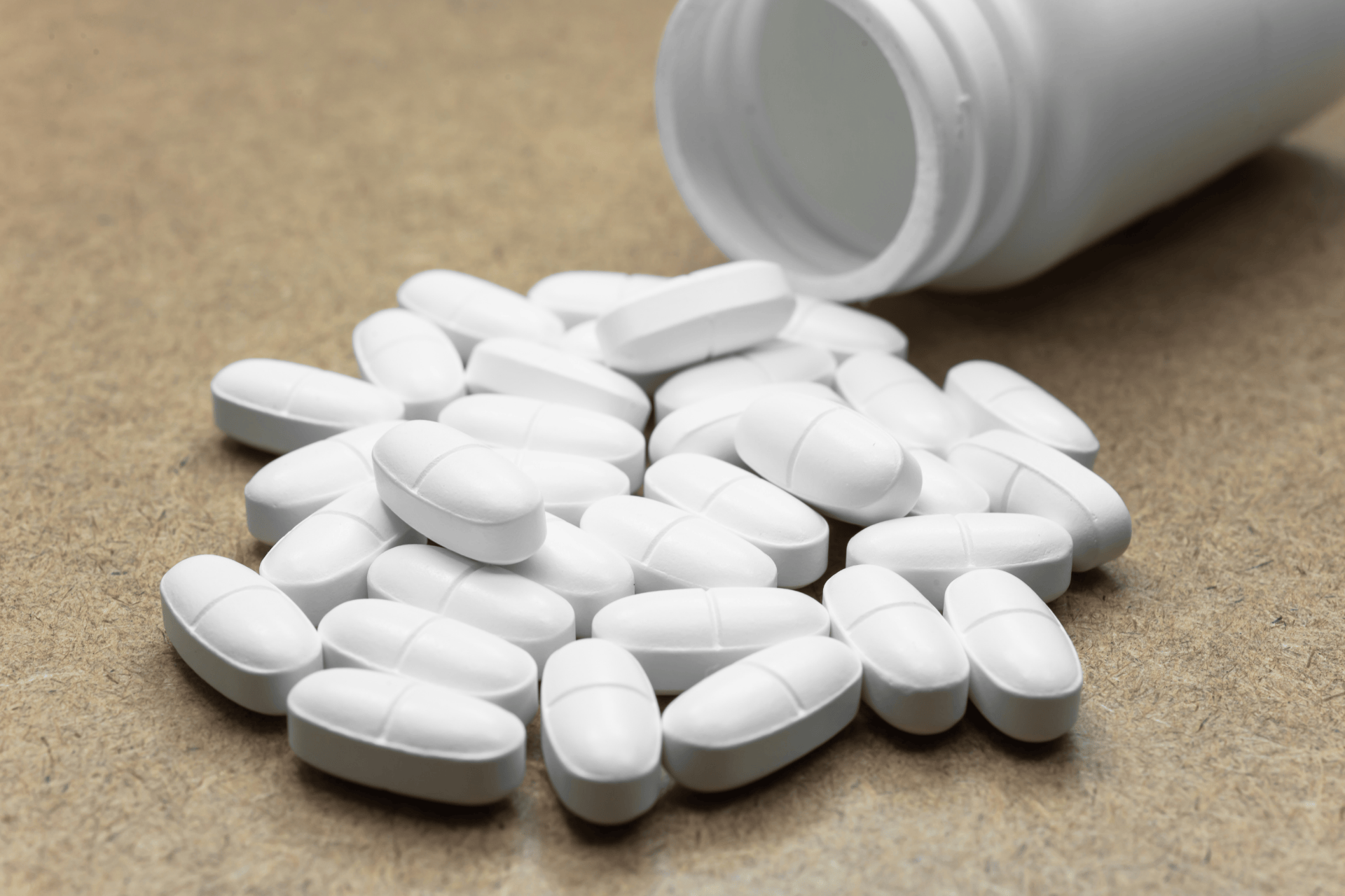 White oval tablets spilled from an open pill bottle onto a surface.