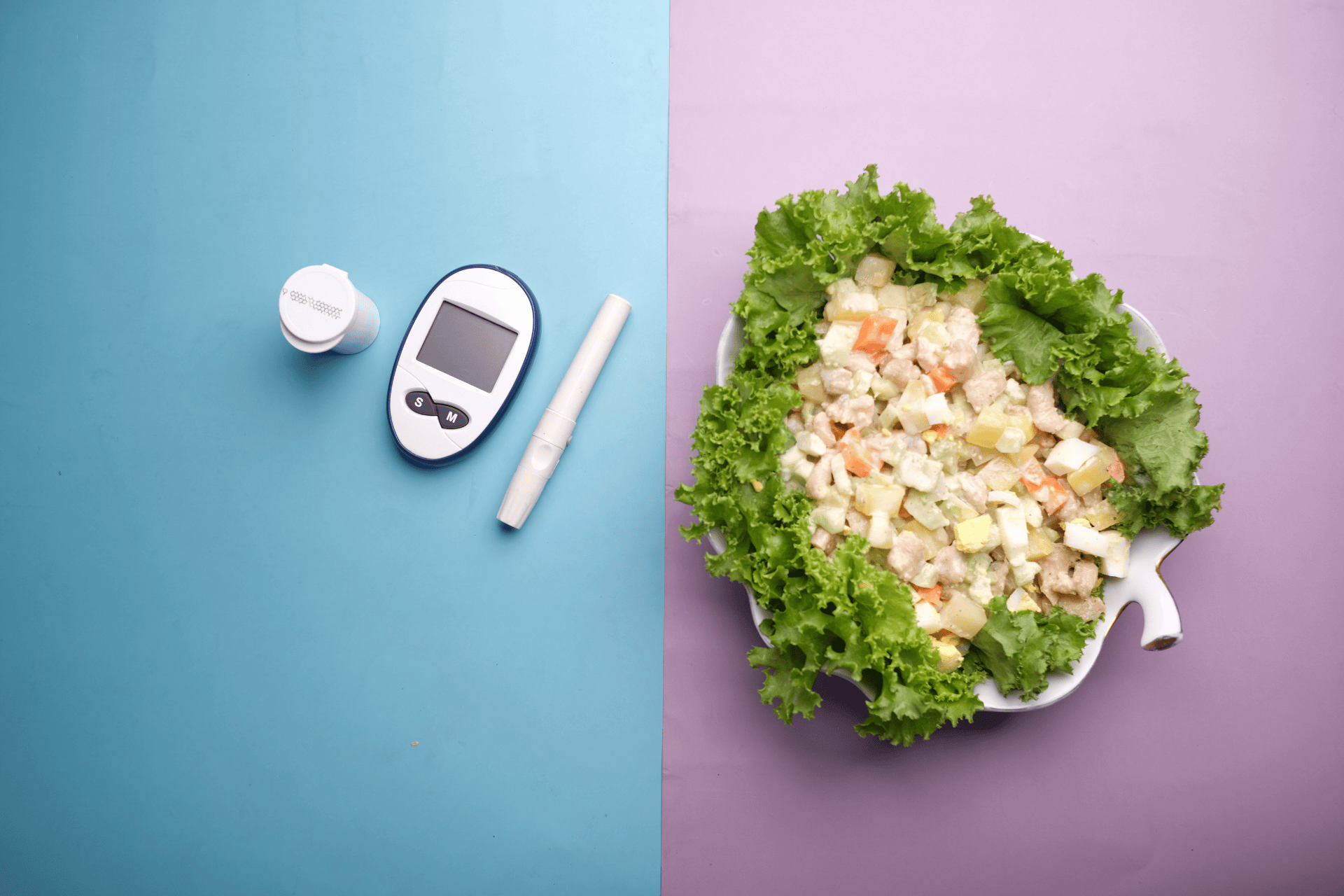 A glucose meter and lancing device beside a bowl of salad on a split blue and purple background.
