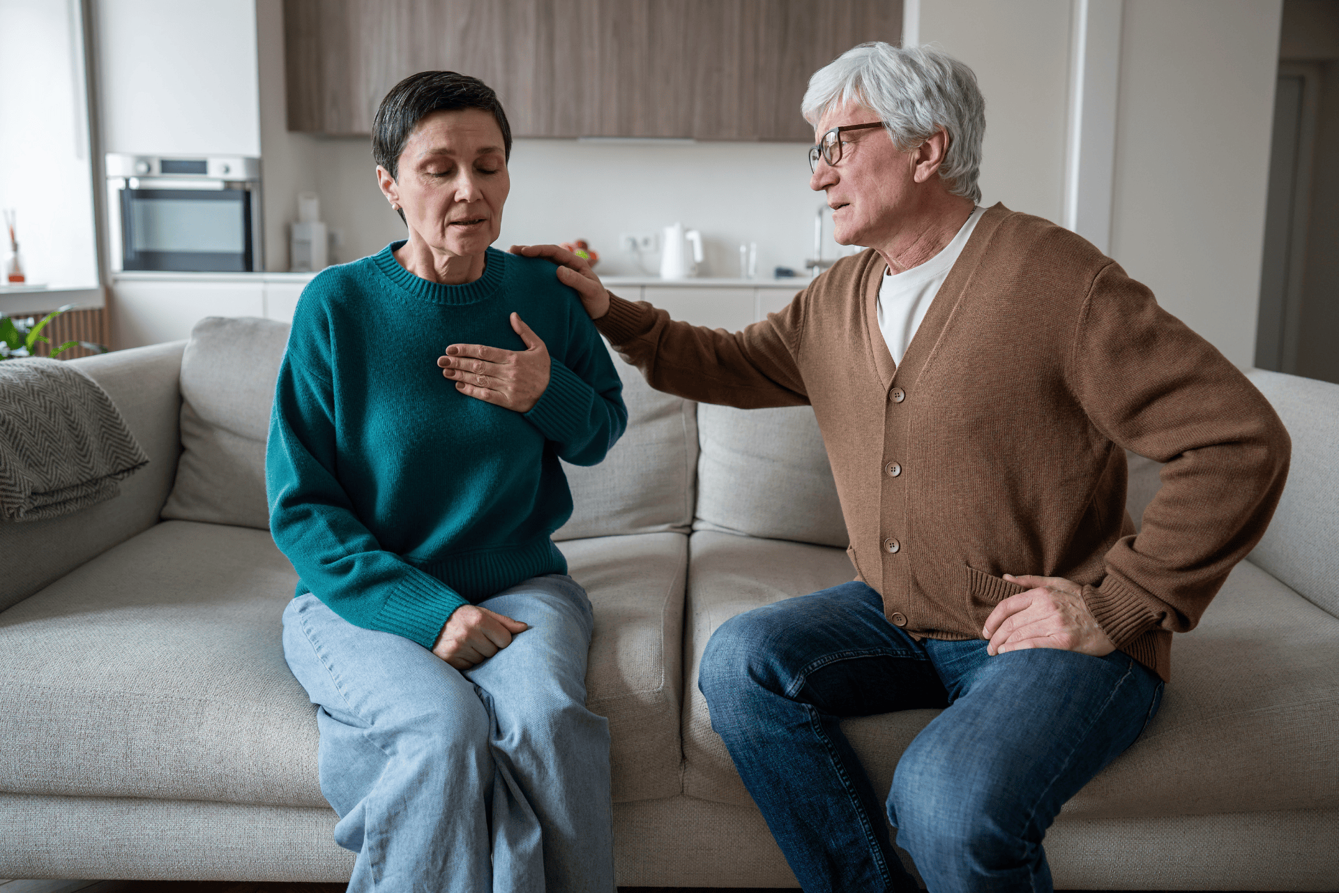 An older woman experiencing heart palpitations while sitting on a couch, supported by her partner.