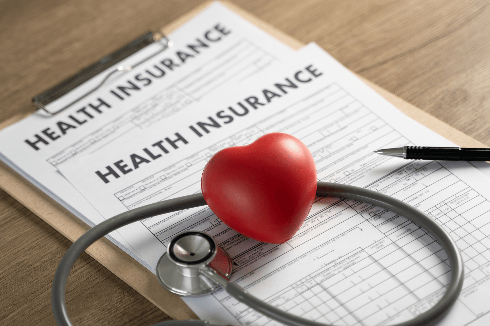 A red heart and stethoscope resting on health insurance forms, symbolizing health coverage.