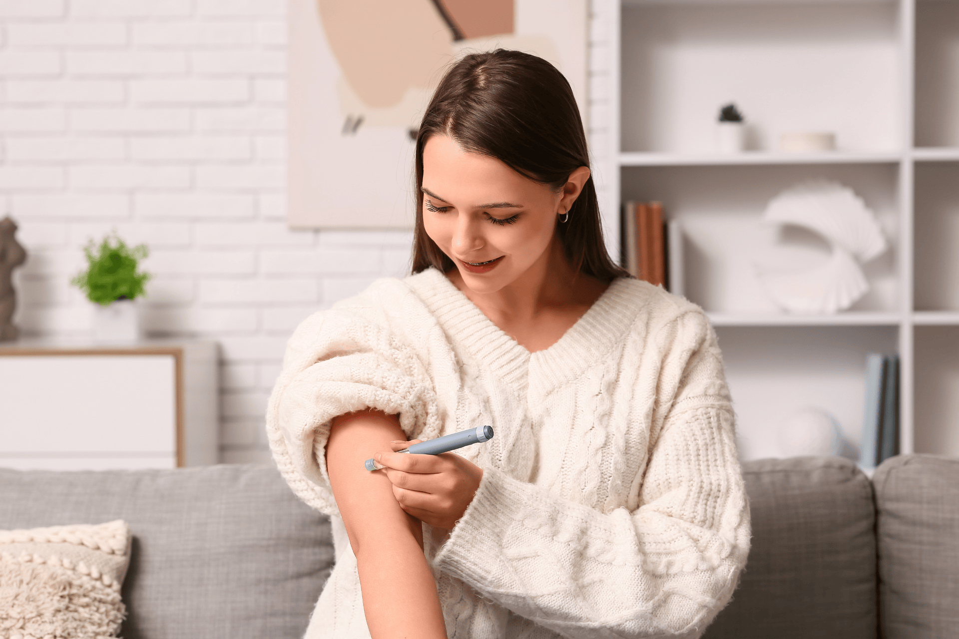 A woman administering an injection into her upper arm at home.