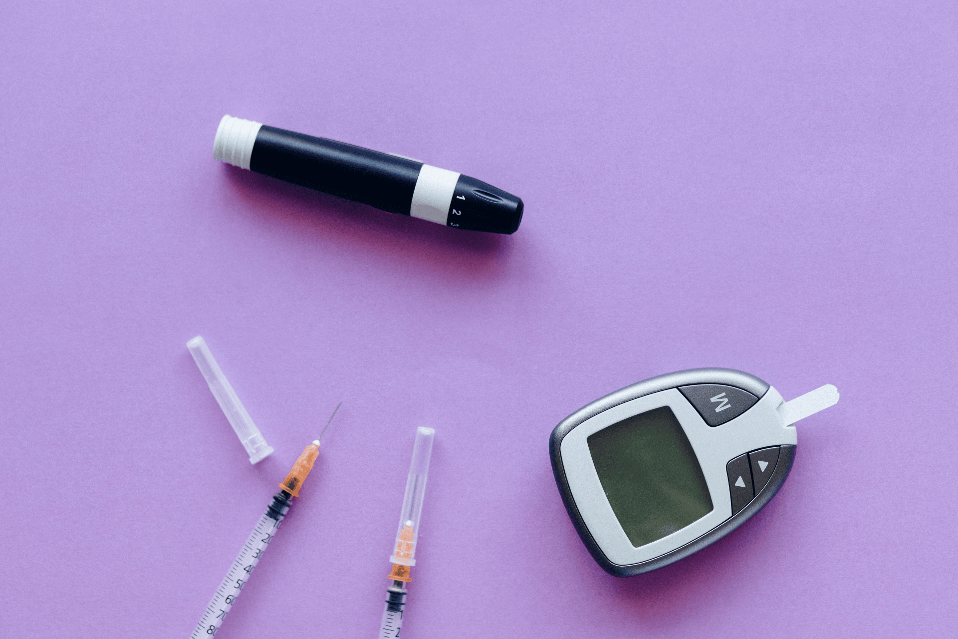 Blood glucose meter, insulin pen, and syringes on a purple background.