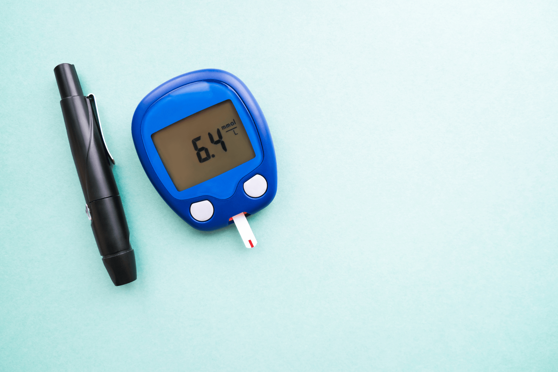 Blood glucose meter displaying a reading of 6.4 mmol/L with a test strip inserted, placed next to a black lancet pen on a light blue background.