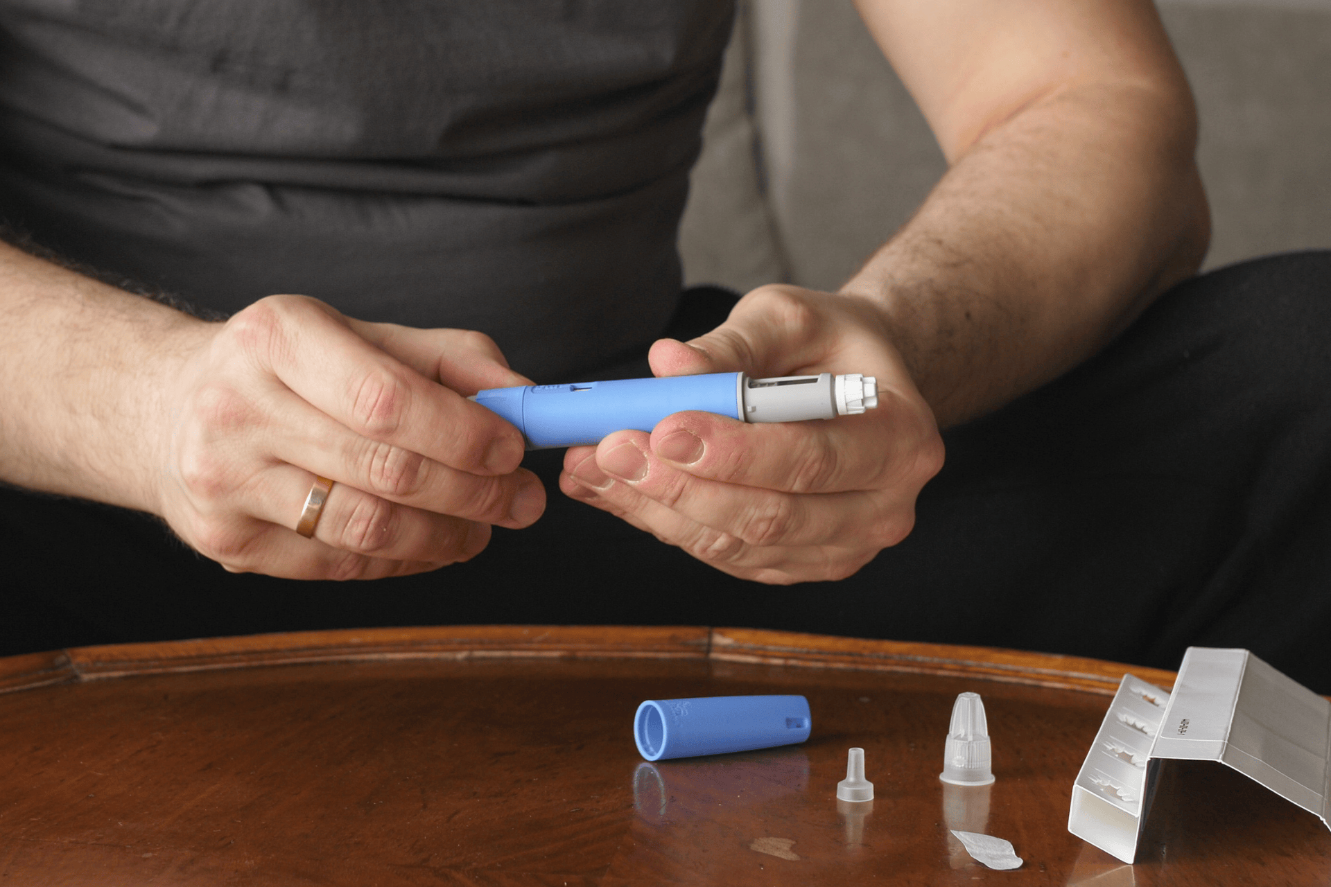 Person holding and assembling an insulin pen at a table, with pen parts and packaging nearby.
