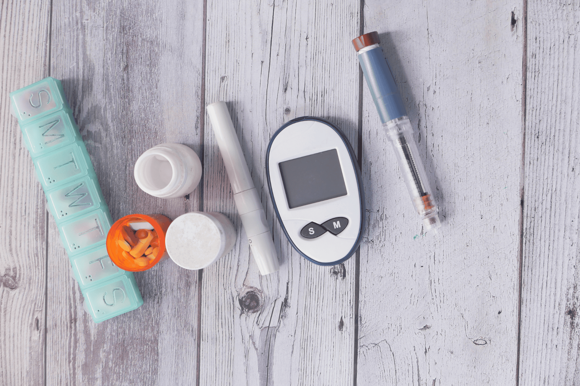 Diabetes management essentials: insulin pen, glucose meter, and daily medications on a wooden surface.