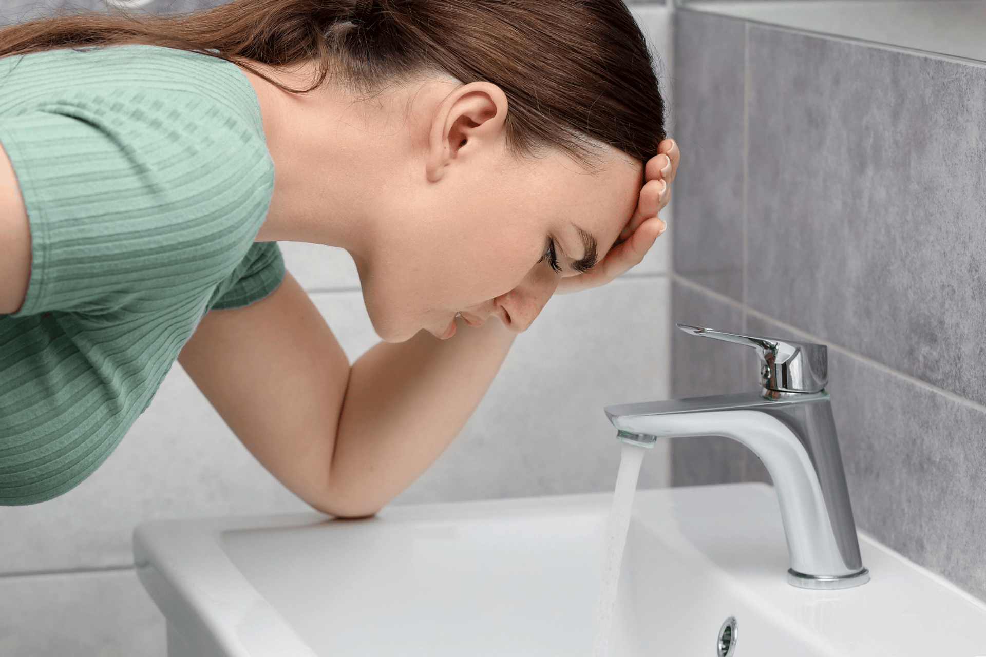 A woman leaning over a sink, feeling nauseous or dizzy, a common sign of nausea, vomiting, or medication side effects.