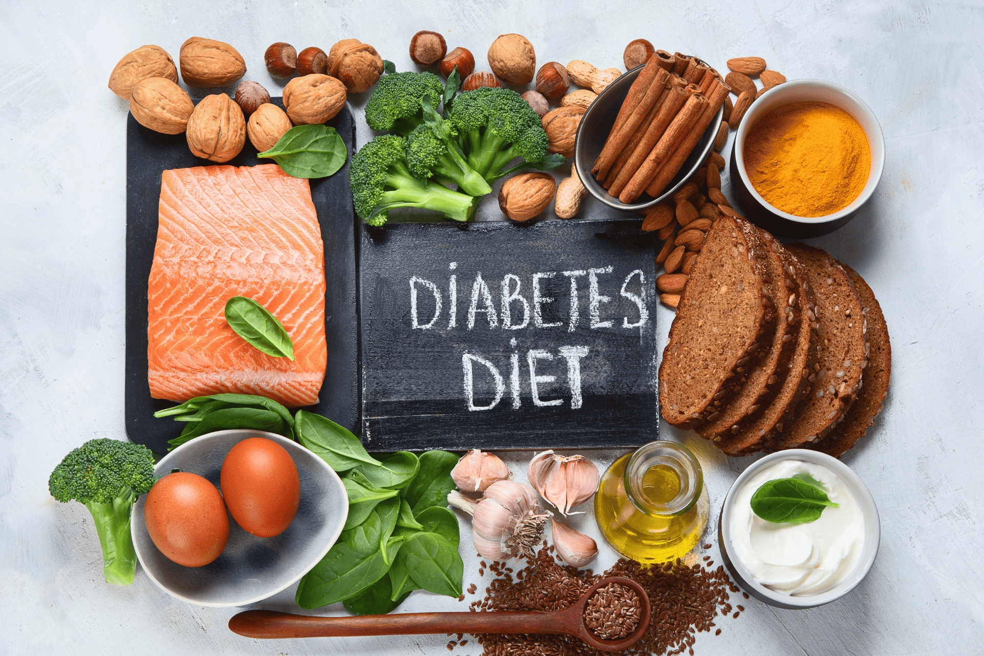 Flat-lay of diabetes-friendly foods around a chalkboard labeled “Diabetes Diet,” including salmon, eggs, vegetables, nuts, whole-grain bread, spices, and olive oil.