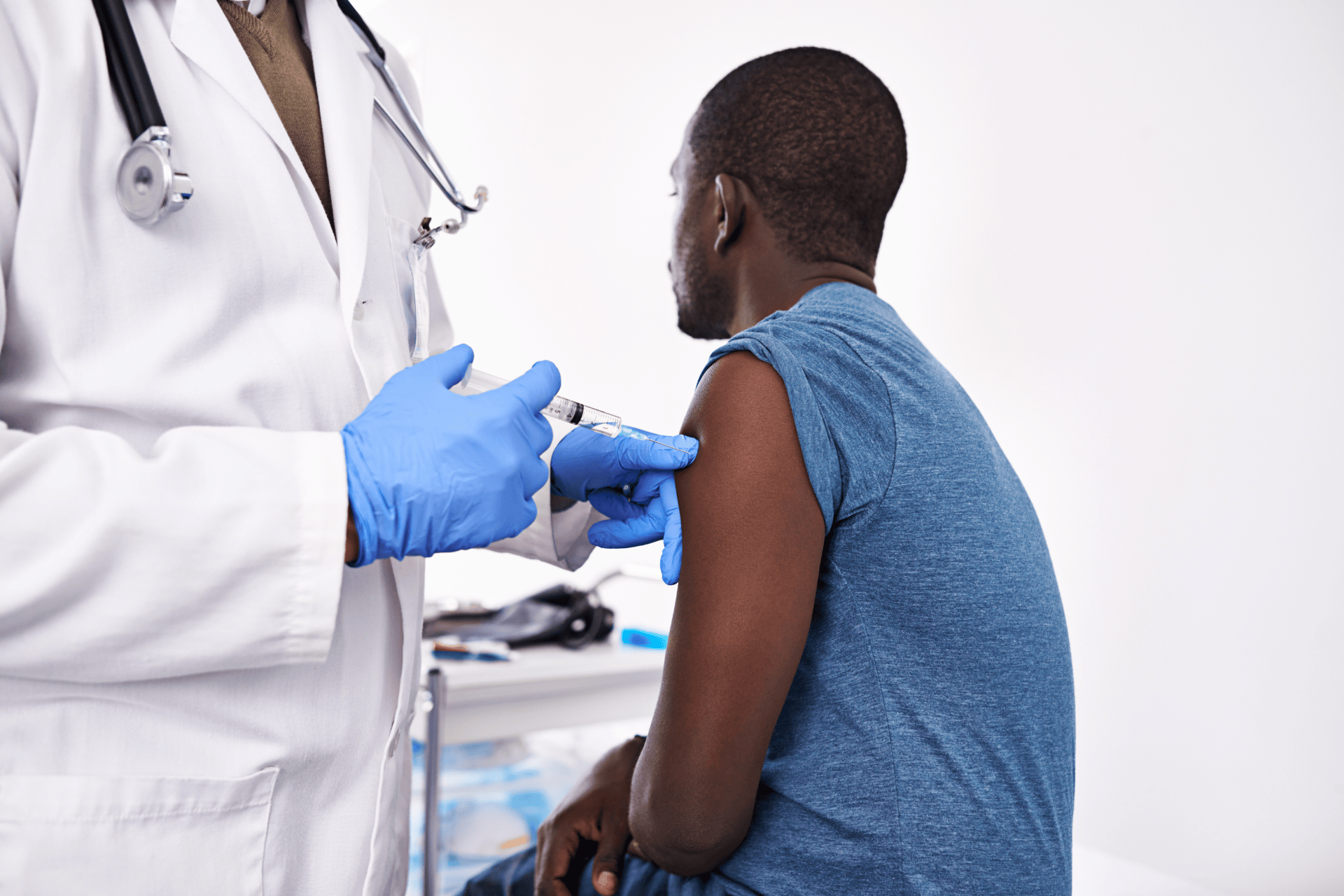 Healthcare provider giving a flu shot to a man’s upper arm in a medical setting.