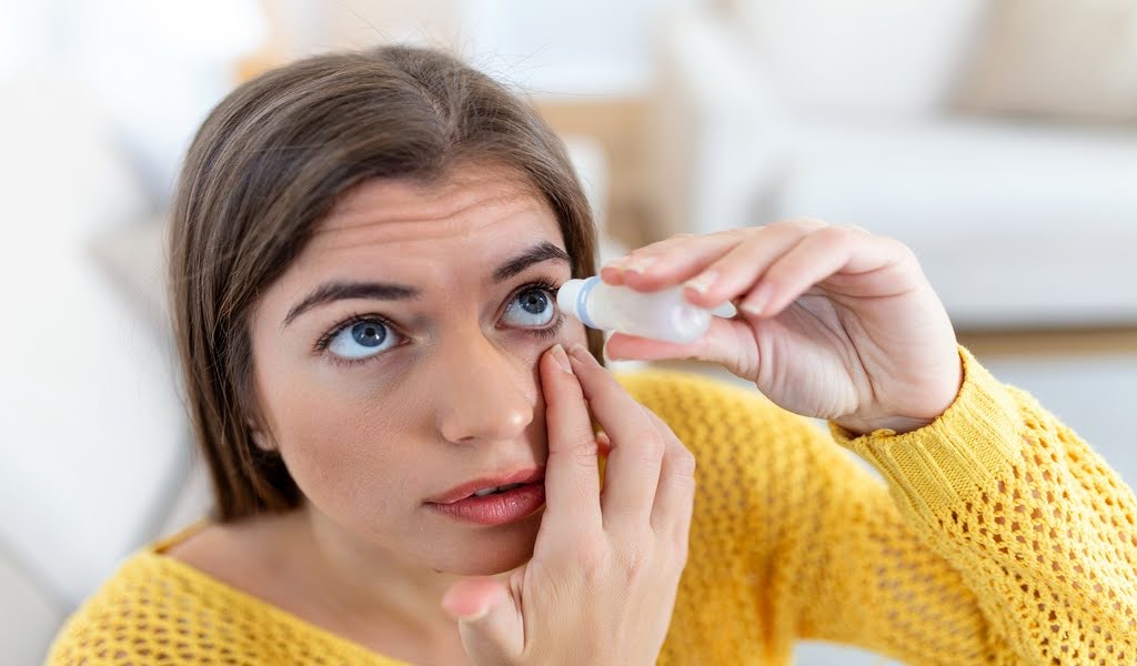 A woman holding an eye drop bottle above her eye