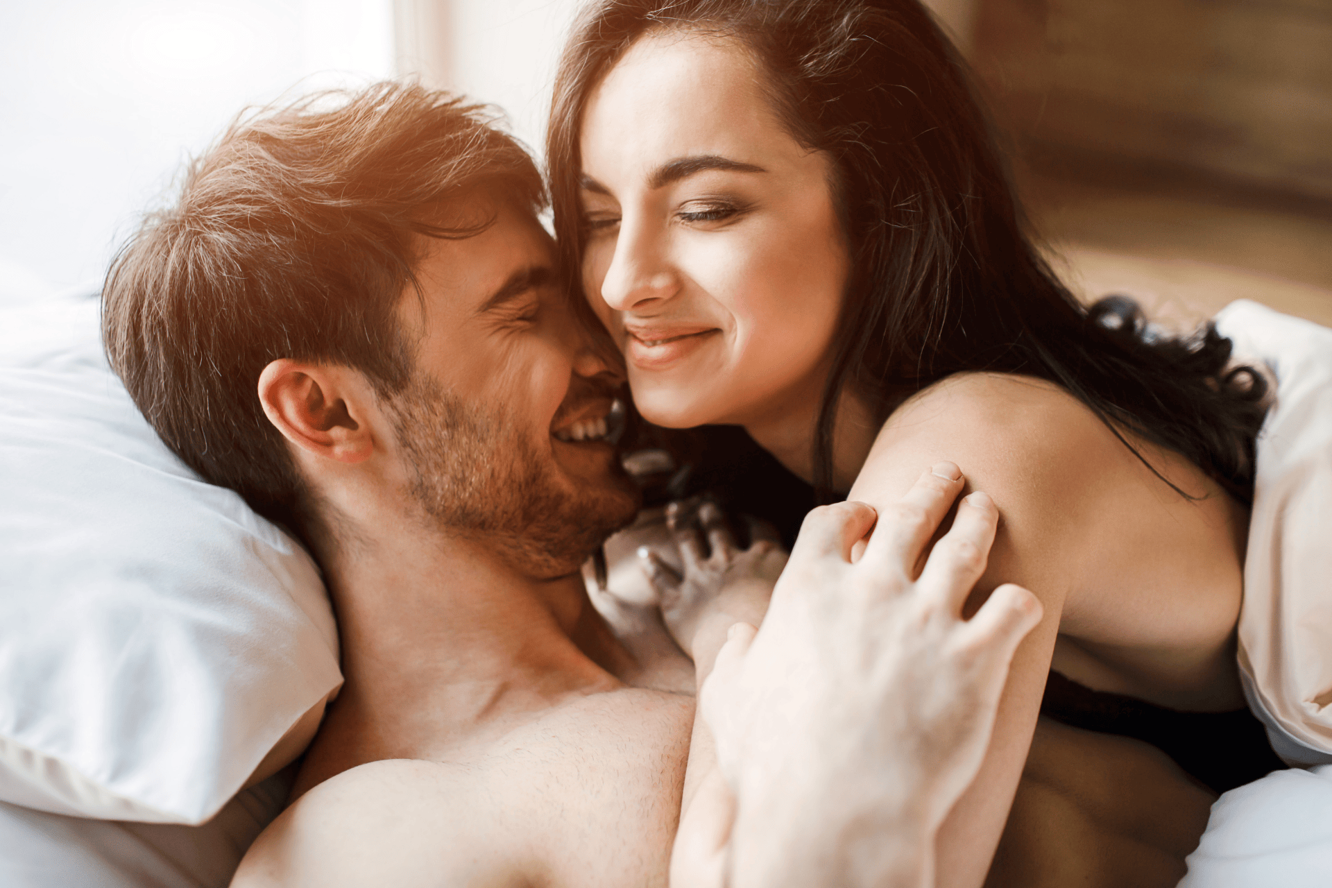A smiling couple cuddling closely in bed, appearing affectionate and happy.