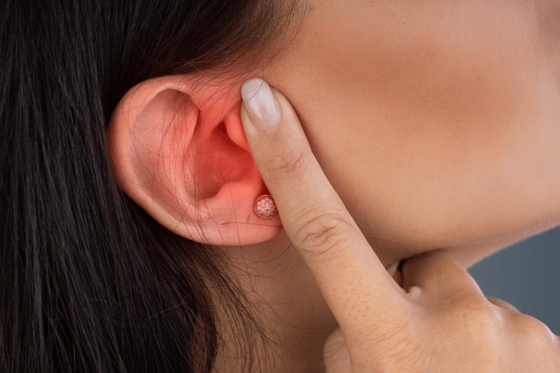 Close-up of a person’s ear with redness and irritation, as they touch the affected area.