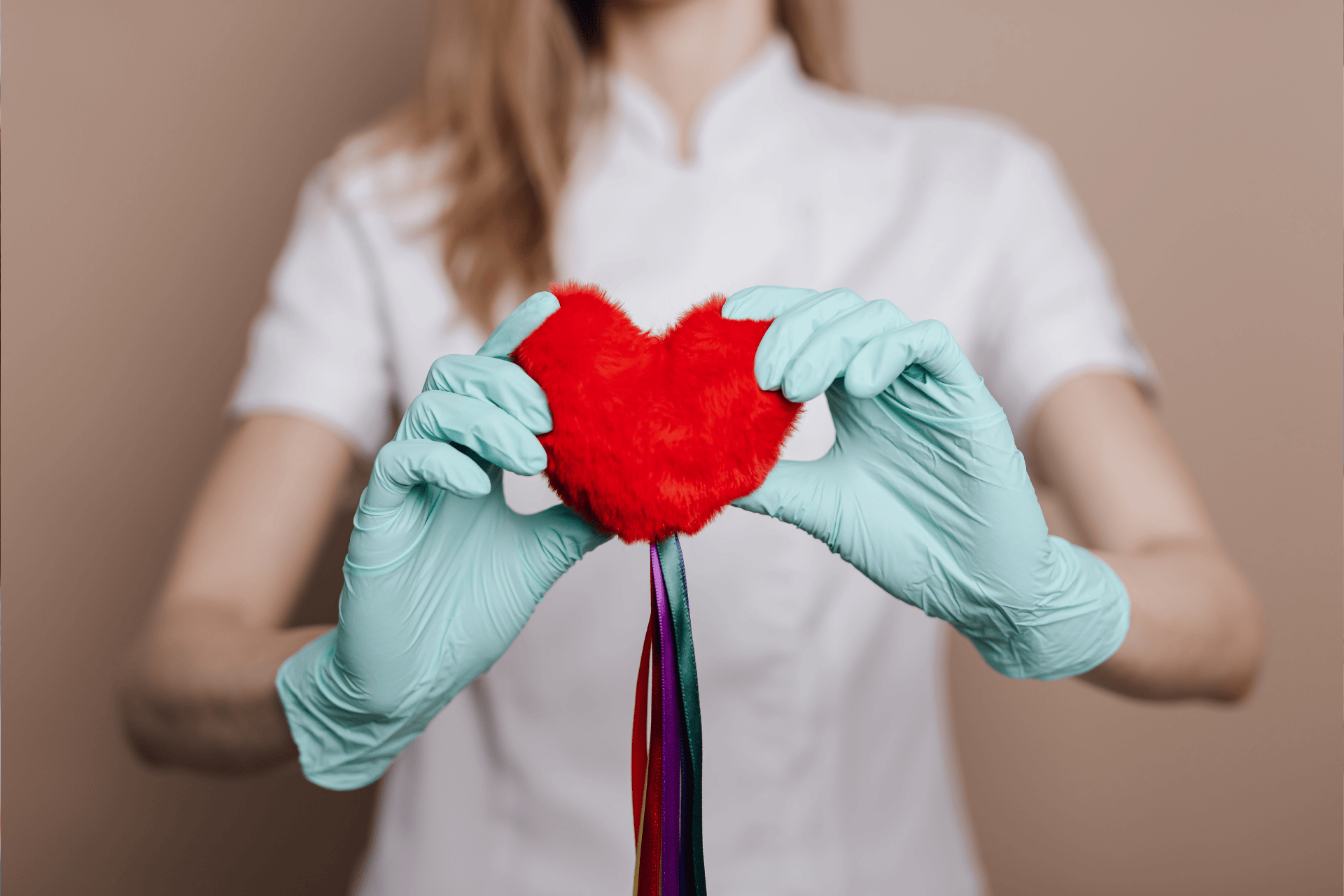 Healthcare professional wearing gloves holding a red heart-shaped object with colorful ribbons.